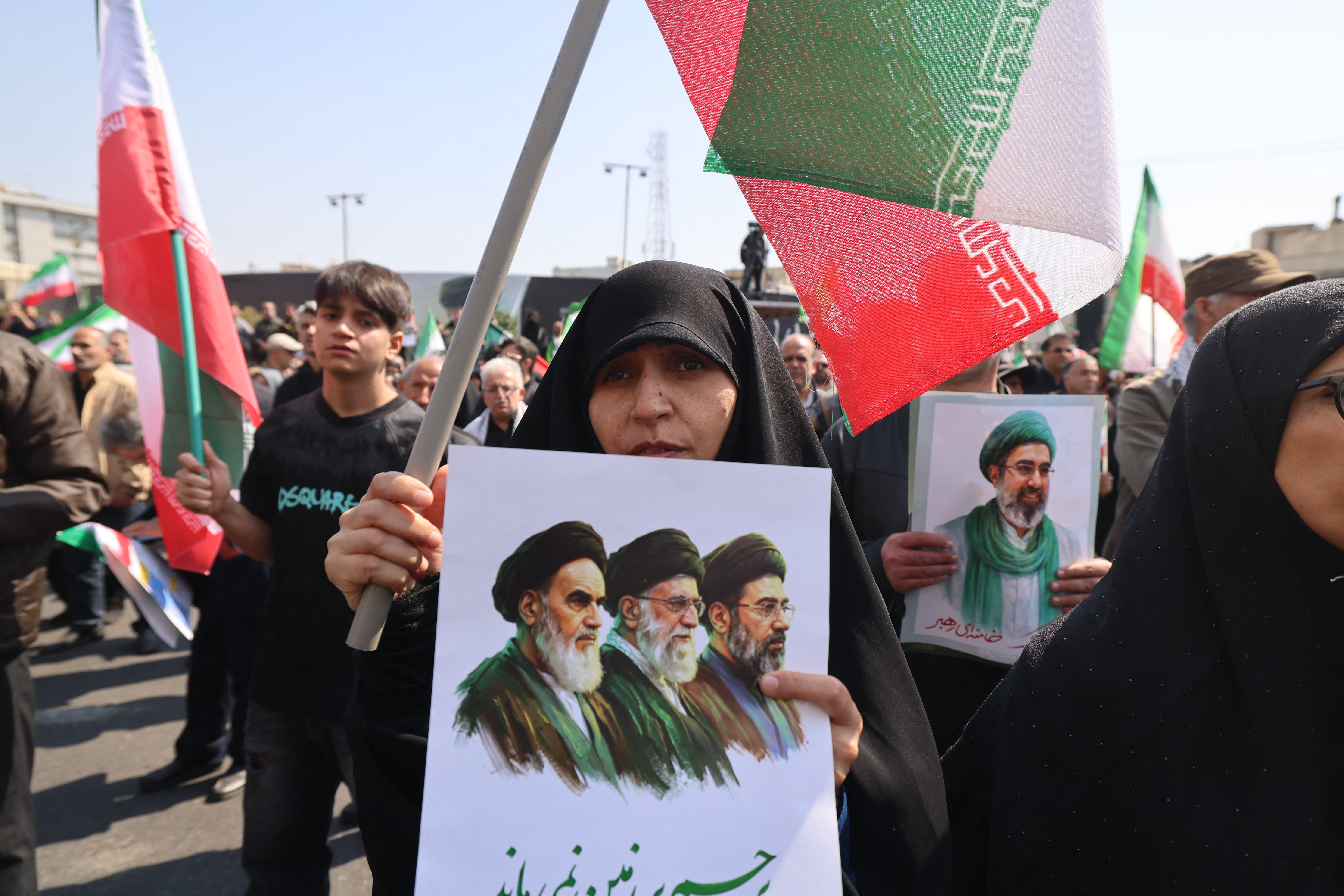 A mourner (C) holds a picture depicting Iran's supreme leaders since 1979: (R to L) Ayatollahs Ruhollah Khomeini (until 1989), Ali Khamenei (until 2026), and Mojtaba Khamenei (incumbent) during the funeral of Iran's security chief Ali Larijani and Gholamreza Soleimani, a senior officer in the Islamic Revolutionary Guard Corps who commands Basij forces, in Tehran on March 18, 2026.