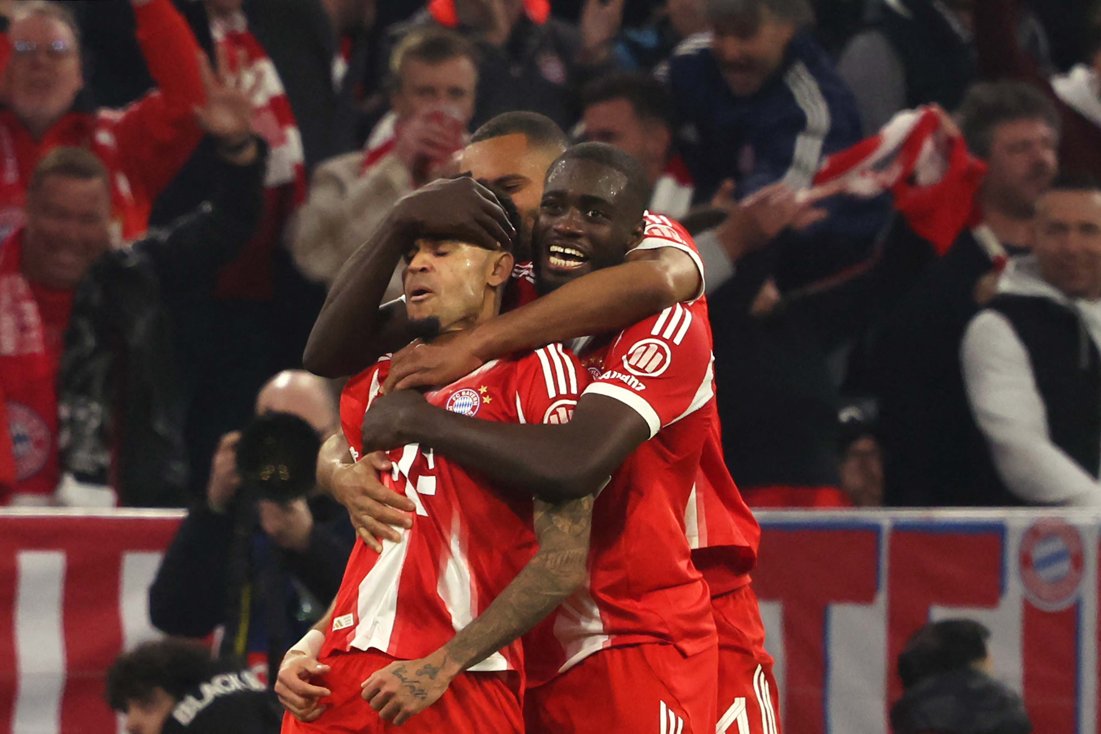 Bayern Munich's Colombian forward #14 Luis Diaz (L) celebrates with Bayern Munich's French defender #02 Dayot Upamecano (R) and Bayern Munich's German defender #04 Jonathan Tah (C)after scoring the equalizing 3-3 goal during the UEFA Champions League quarter-final second leg football match between FC Bayern Munich and Real Madrid in Munich, southern Germany, on April 15, 2026.