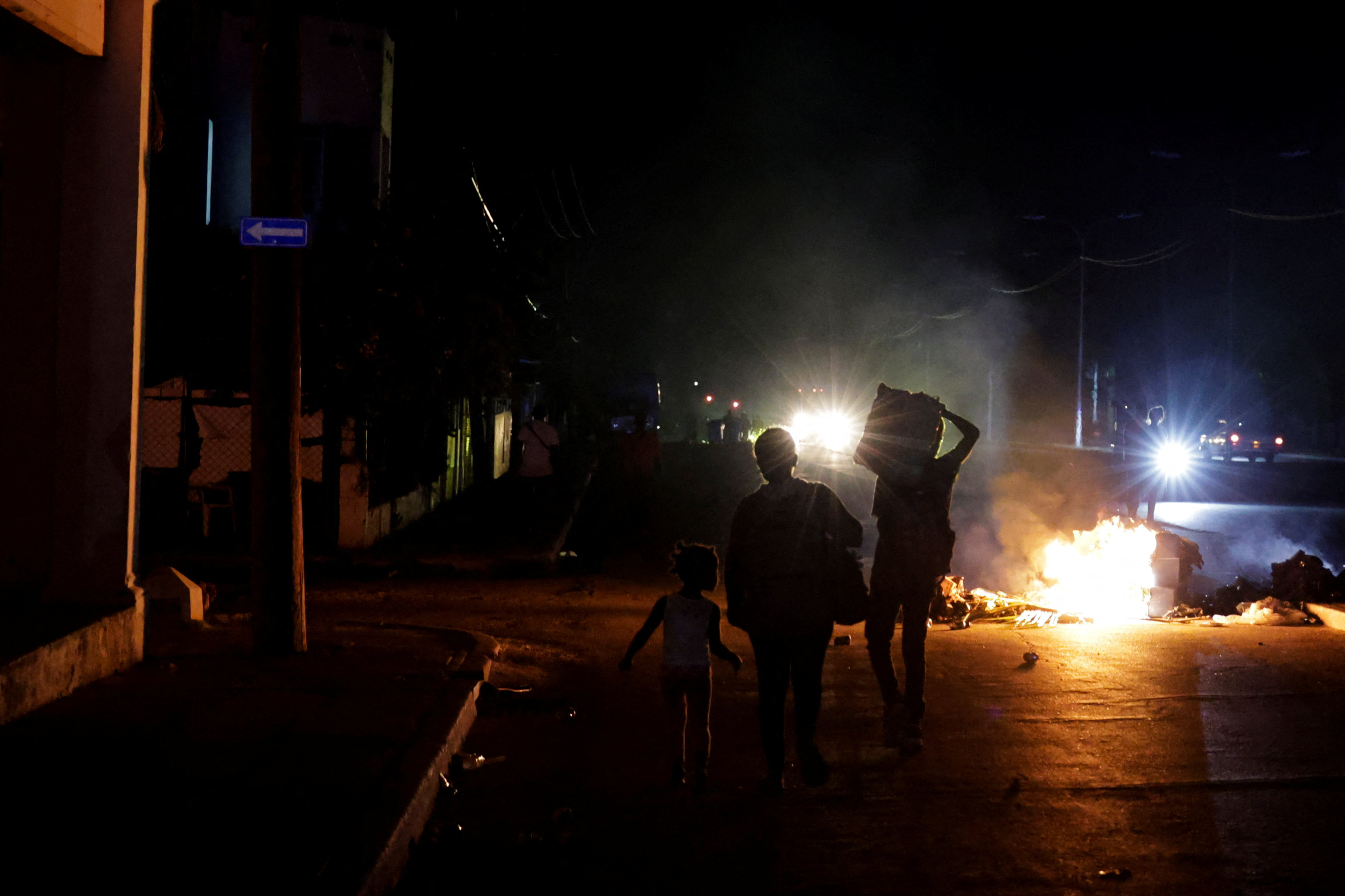 People walk past trash set on fire in the middle of a street during a protest against frequent power cuts as Havana faces its worst rolling blackouts in decades