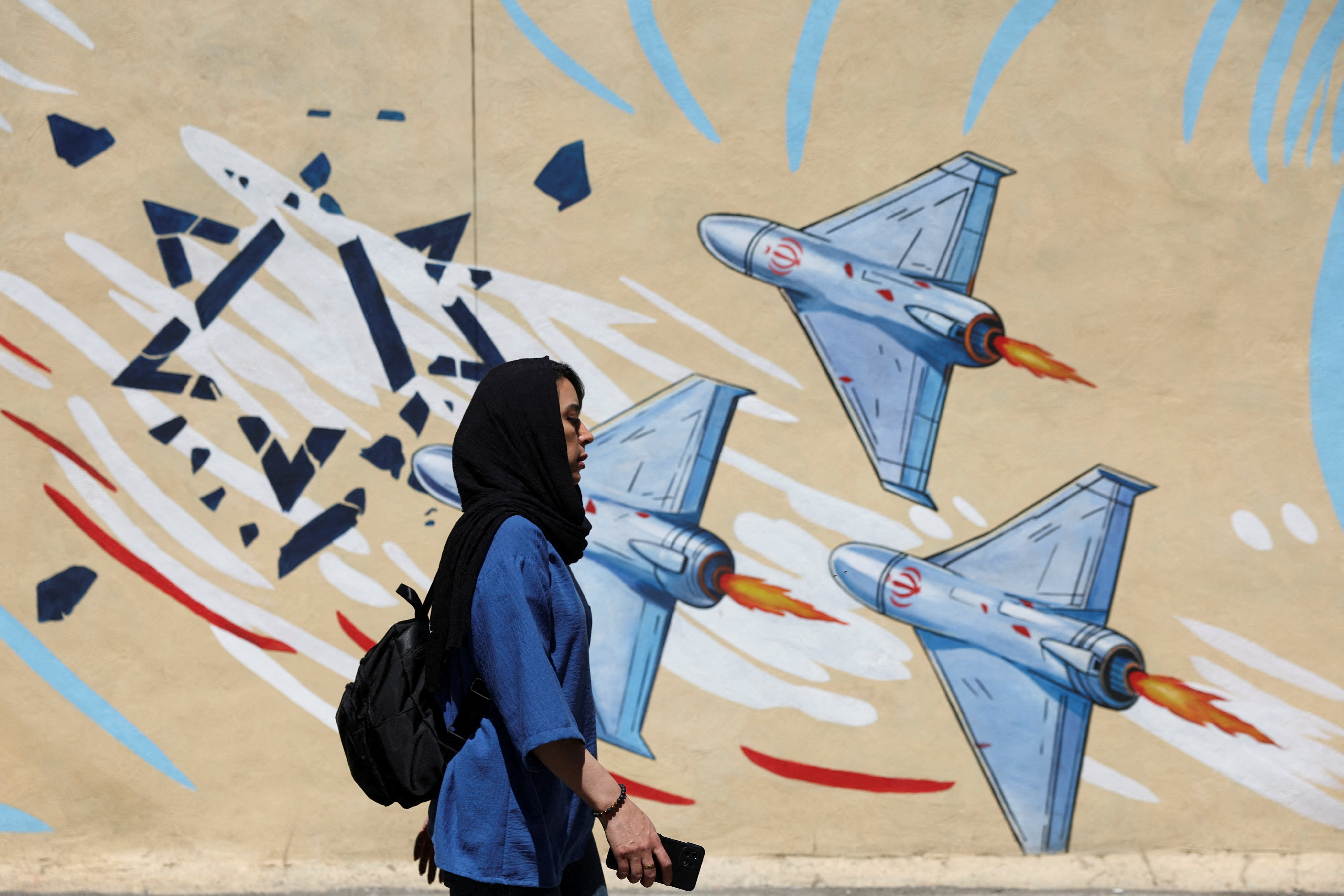 Woman walks next to mural of Iranian drones