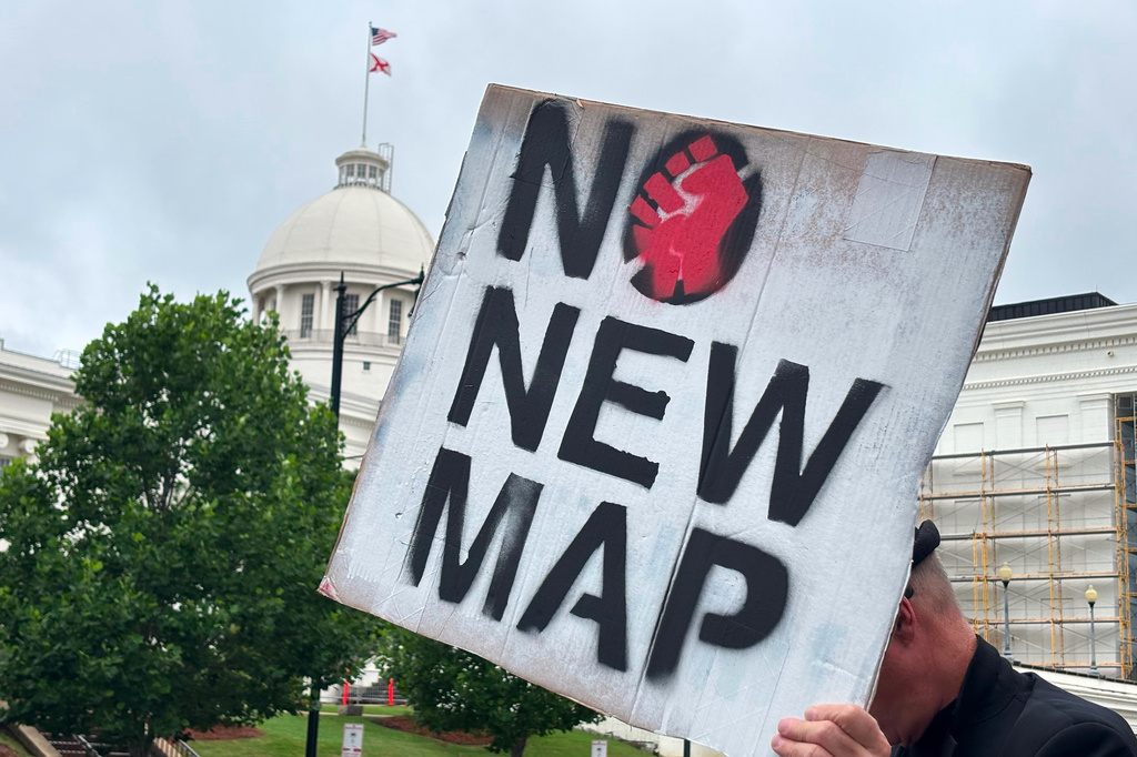 a demonstrator holds a placard opposing gerrymandering stating 'no new map'