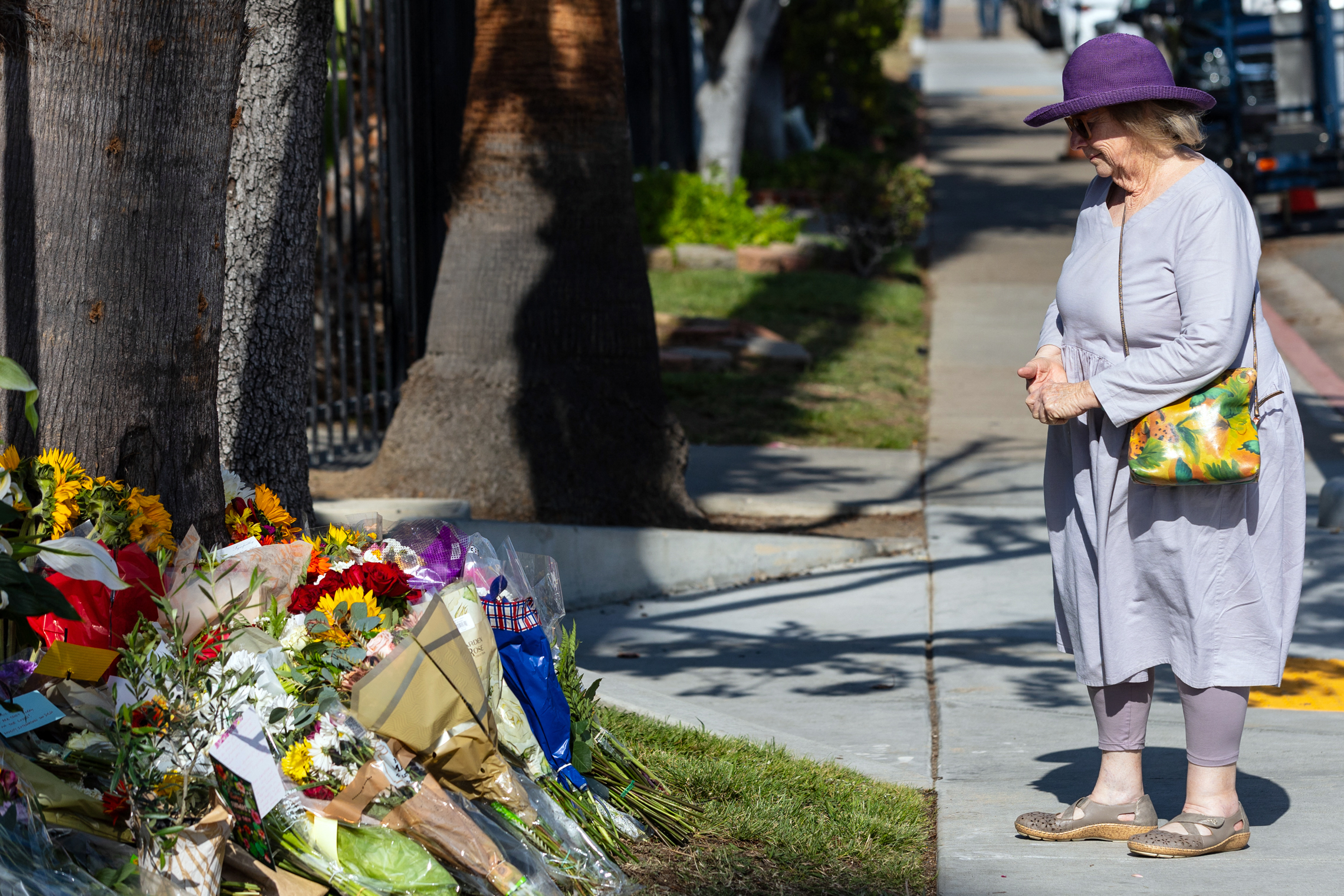 A woman stands next to a tree with many bouquets lying on the ground.