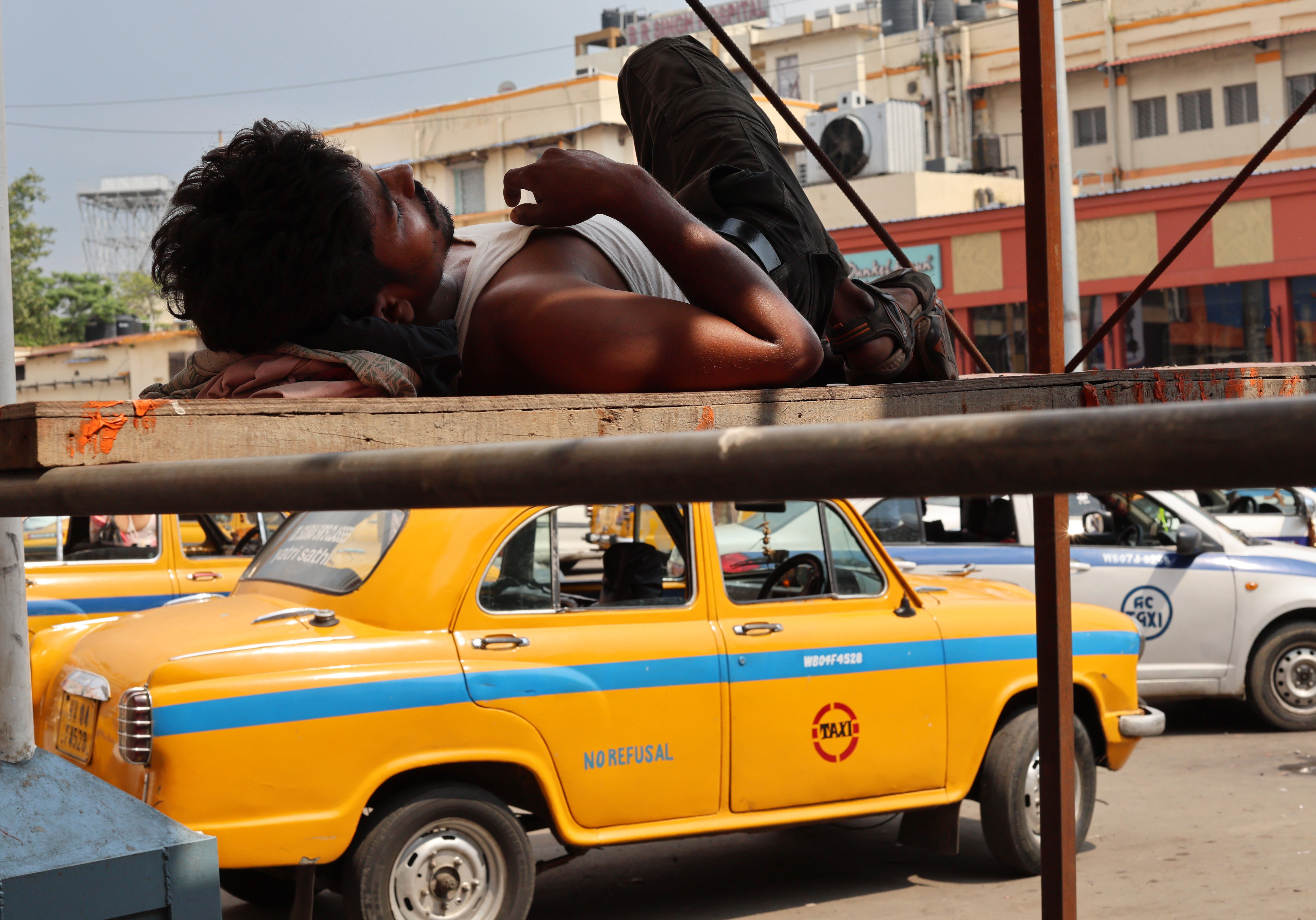epa12936244 An Indian worker rests on scaffolding as a taxi drives by near a market during a hot afternoon in Kolkata, India, 06 May 2026. The India Meteorological Department (IMD) has forecast temperatures to reach up to 38 degrees Celsius as a heat wave persists across West Bengal. EPA/PIYAL ADHIKARY