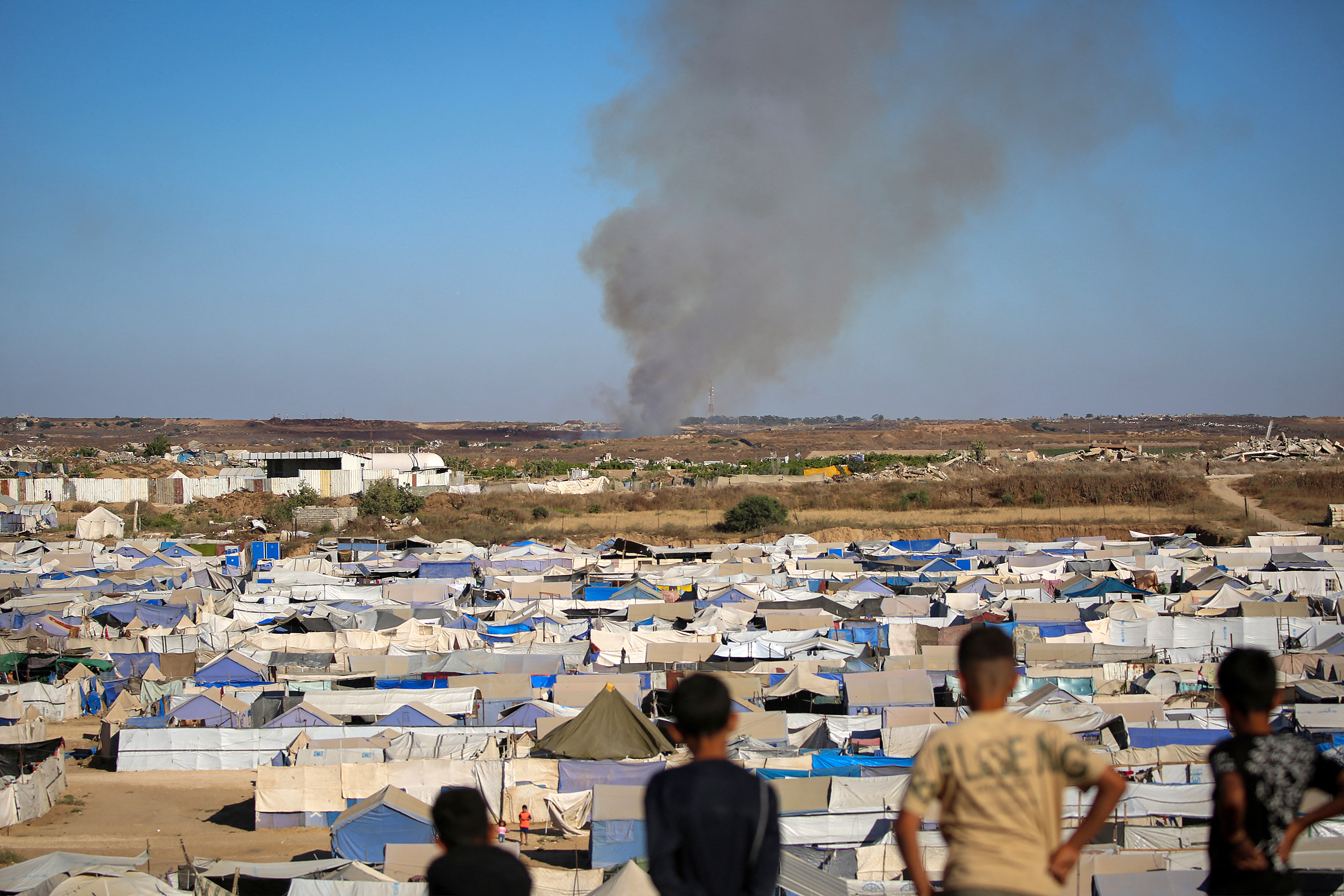 TOPSHOT - Children watch from atop a promontory overlooking shelters for people displaced by war, as smoke billows in the background near the Nuseirat camp for Palestinian refugees in the central Gaza Strip on June 19, 2026.