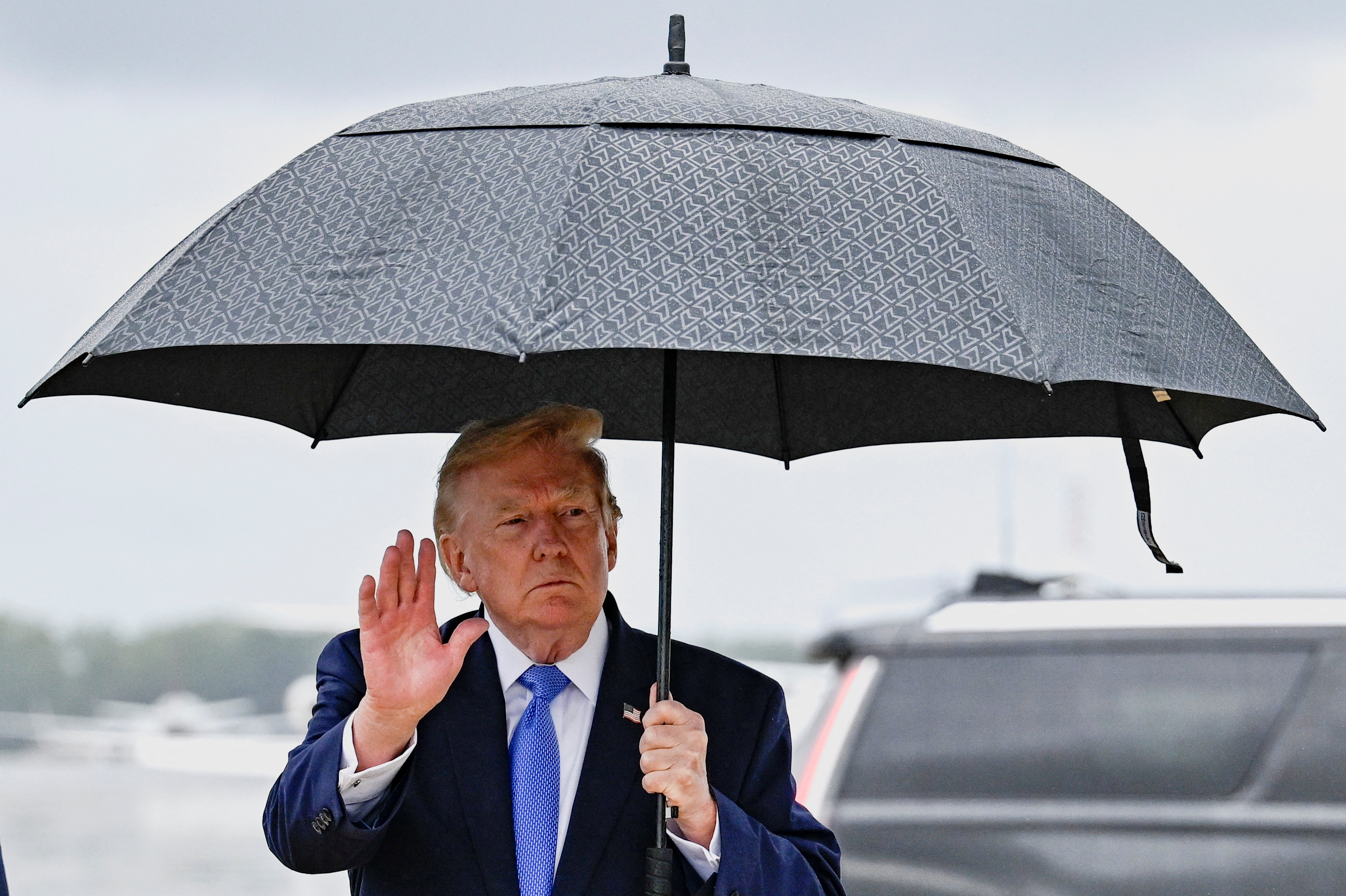 U.S. President Donald Trump gestures as he holds an umbrella after disembarking Air Force One at Joint Base Andrews, in Maryland, US. [Daniel Heuer/Reuters]