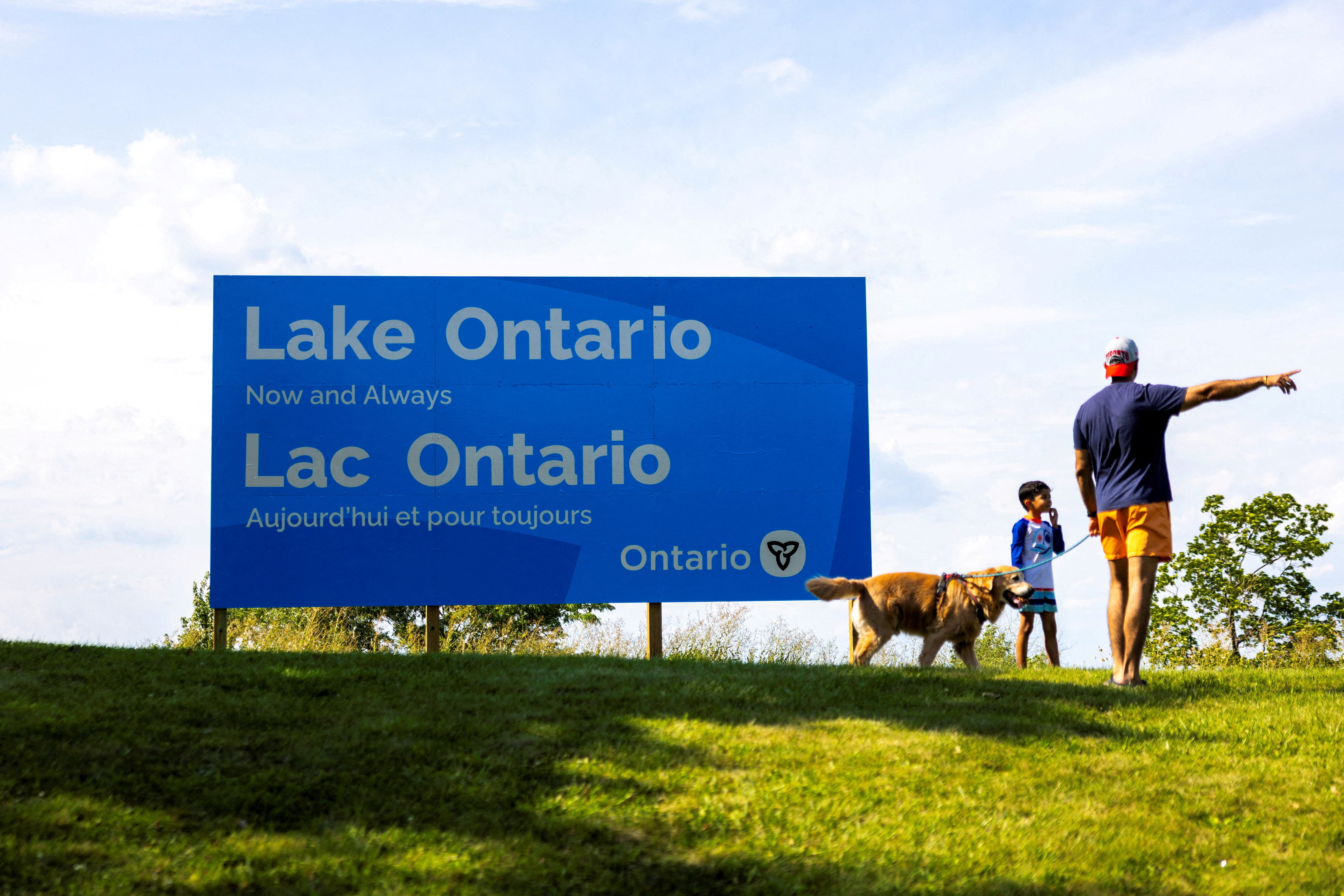 A family walks past a sign reading ‘Lake Ontario, Now and Always’, unveiled by Ontario Premier Doug Ford at Fifty Point Conservation Area near Grimsby, Ontario, Canada, on August 29, 2026, after US President Donald Trump ordered the lake renamed ‘Lake America’
