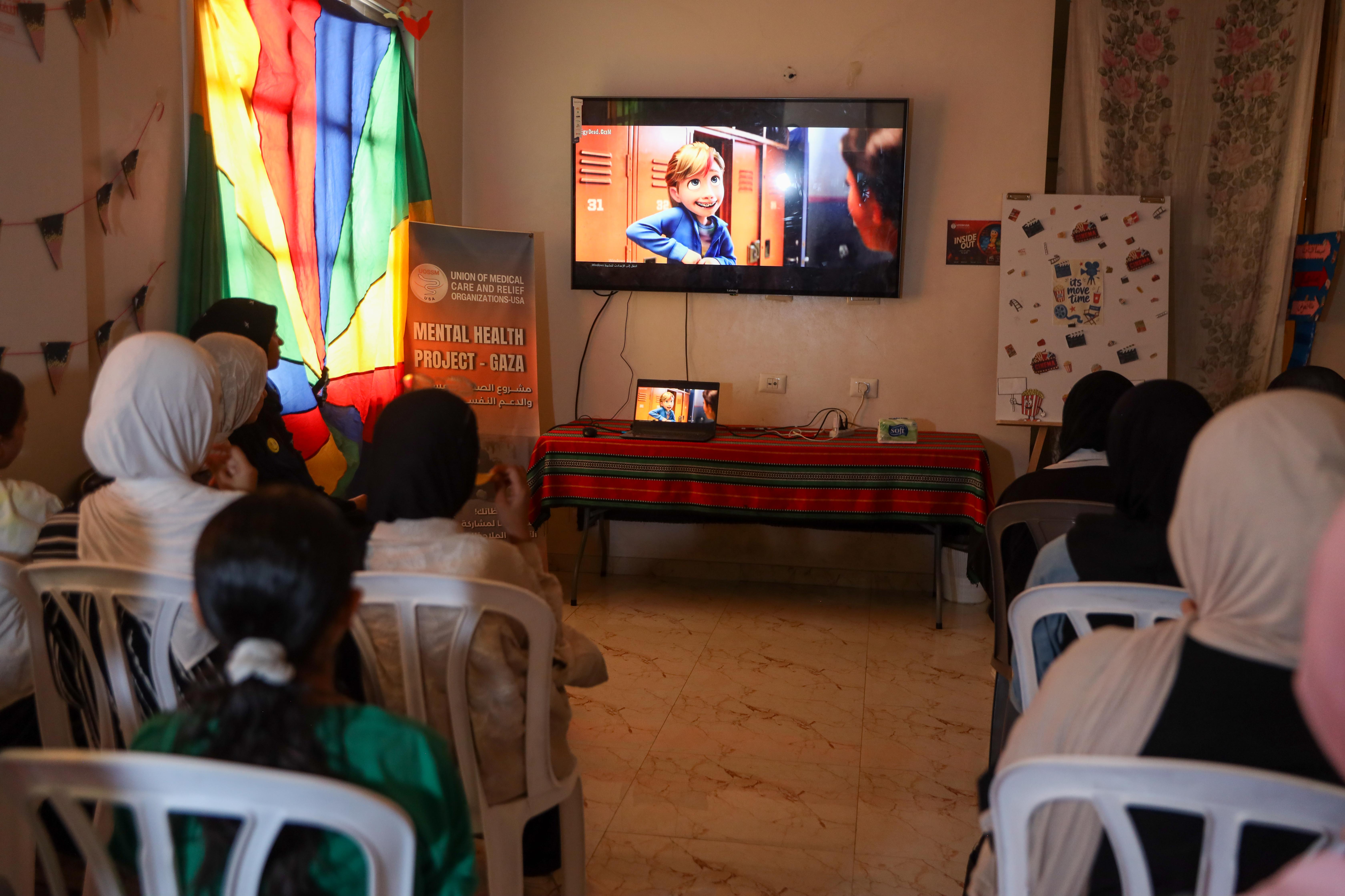 Displaced girls watch an animated film during a weekly cinema activity in Deir al-Balah, Gaza, designed to give them an escape from war [Abdelhakim Abu Riash/ Al Jazeera]