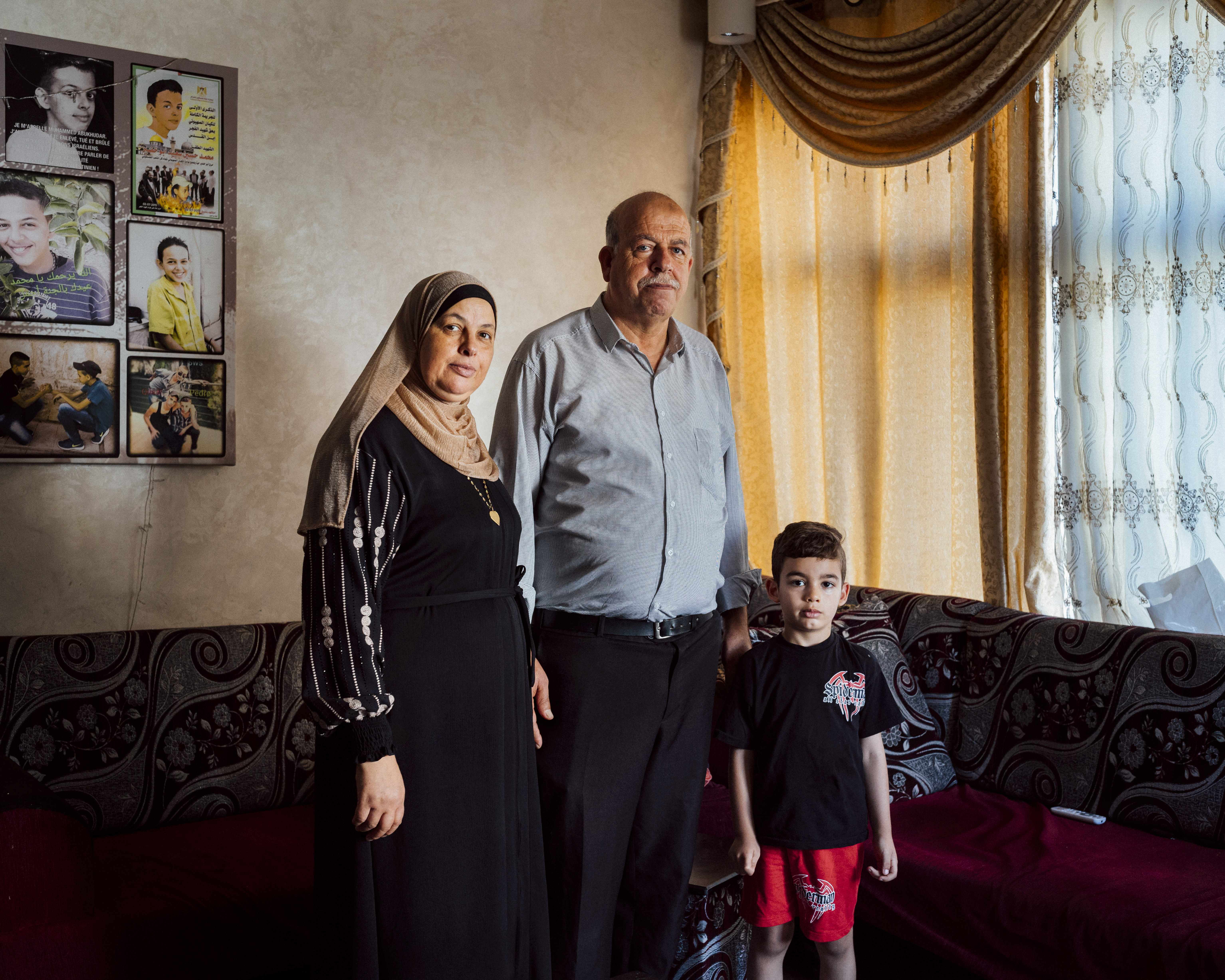 Suha and Hussein Abu Khdeir, parents of Mohammed Abu Khdeir, stand for a portrait alongside their grandchild Azzedine, in the living room of their house in Shuafat neighbourhood of Occupied East Jerusalem. Mohammed was kidnapped outside his home and murdered by Israeli Jewish citizens on July 2nd 2014 [Lucien Lung/Al Jazeera]