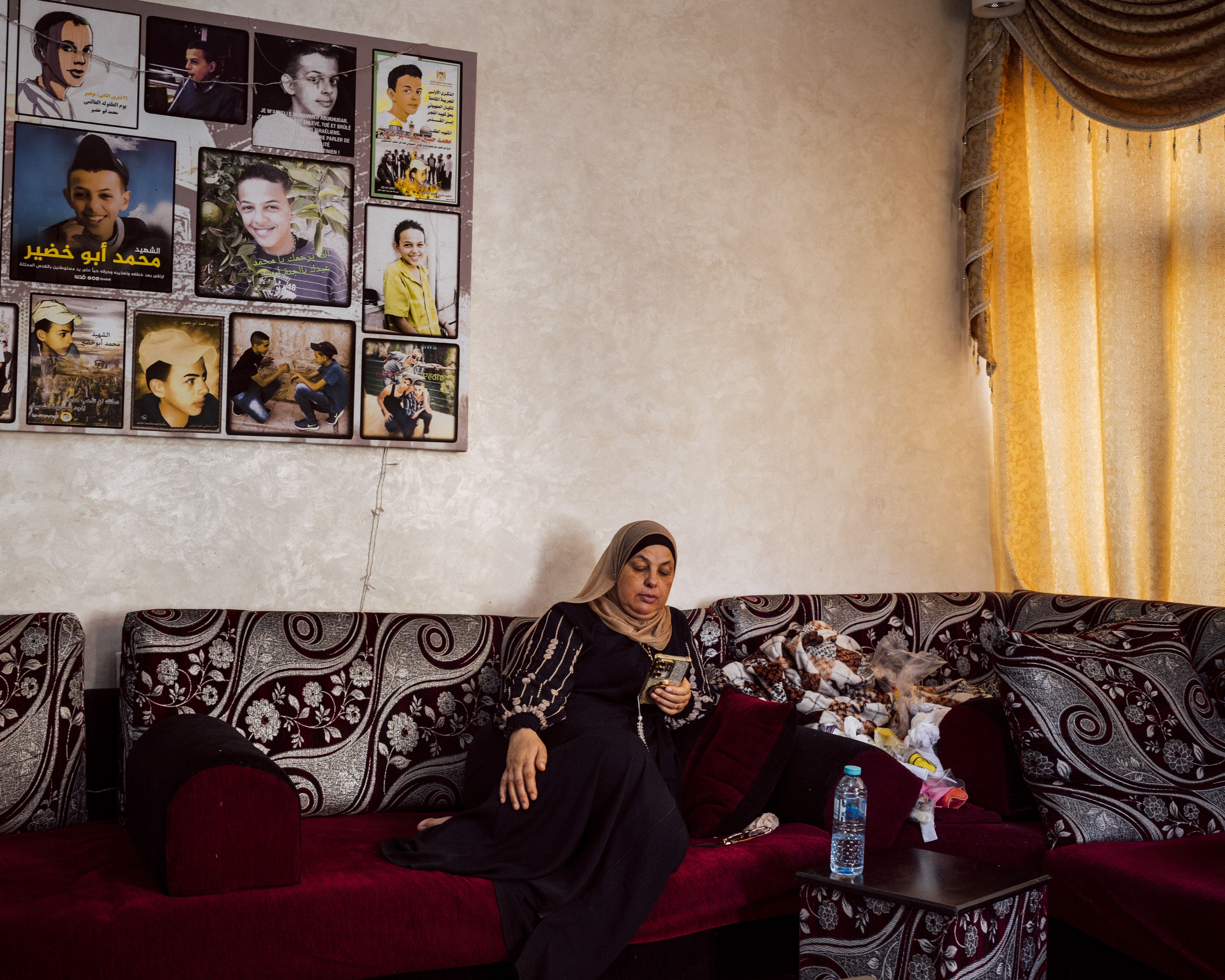 Suha Abu Khdeir sits underneath pictures of Mohammed Abu Khdeir in the living room of her home, in Shuafat neighbourhood of Occupied East Jerusalem. Mohammed was kidnapped outside his home and murdered by Israeli Jewish citizens on July 2nd 2014 [Lucien Lung/Al Jazeera]