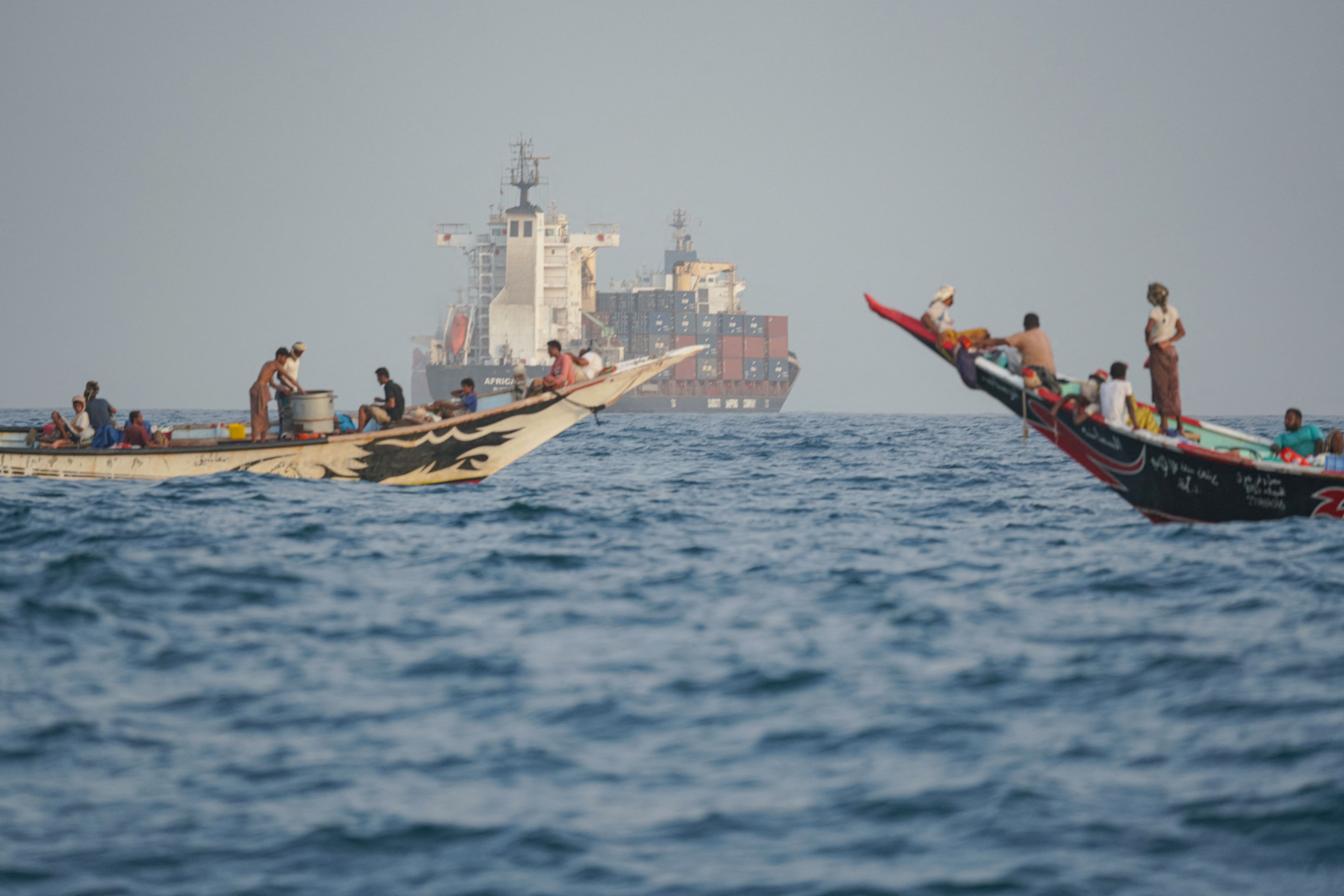 People sail their boats past container ships.