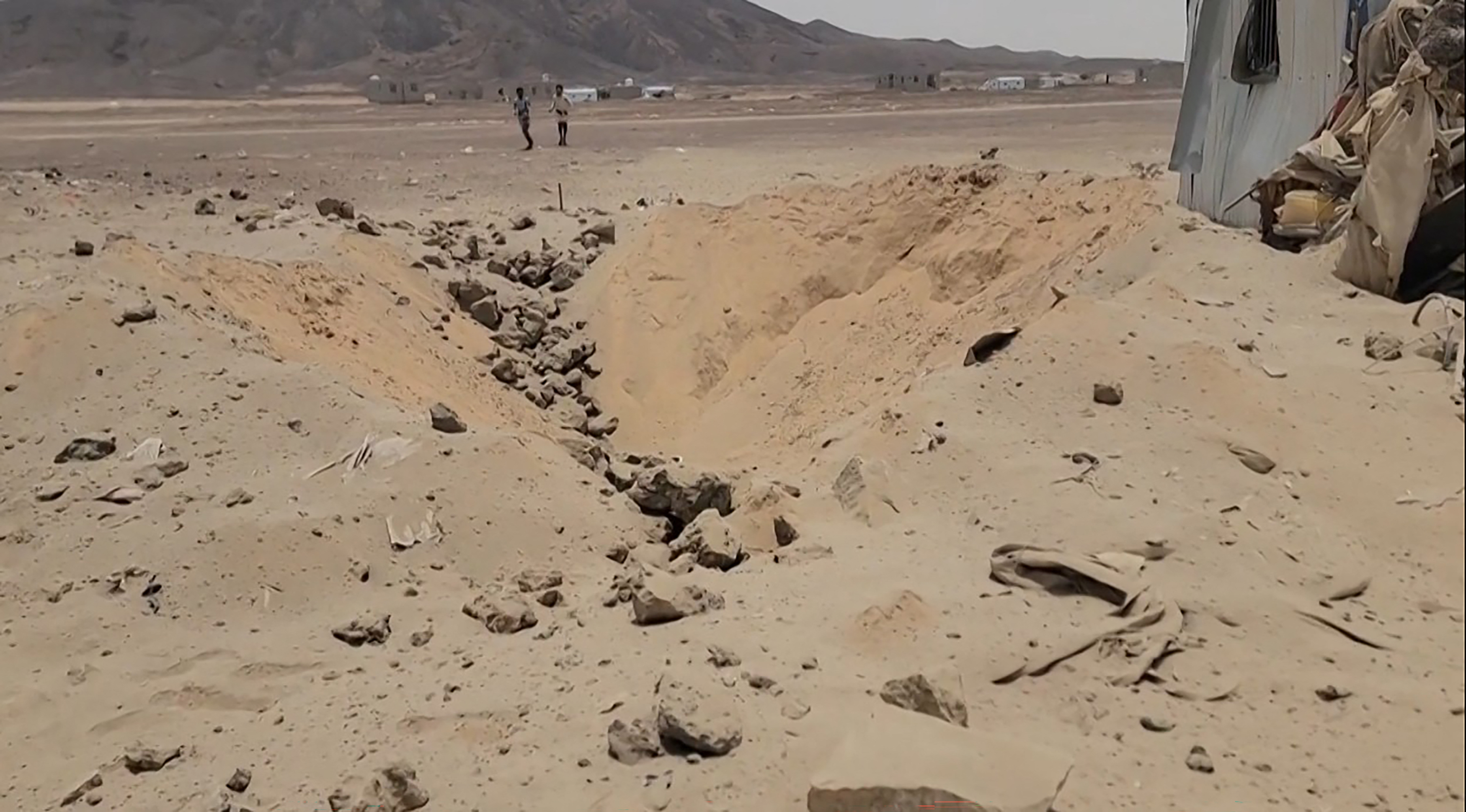 This frame grab taken from AFPTV video footage on August 7, 2026, shows people walking near the damage at Mail al-Saila internally displaced camp (IDP) on the outskirts of Marib following a reported Houthi ballistic missile attack on the government-held city of Marib early August 7, amid an escalation in hostilities.