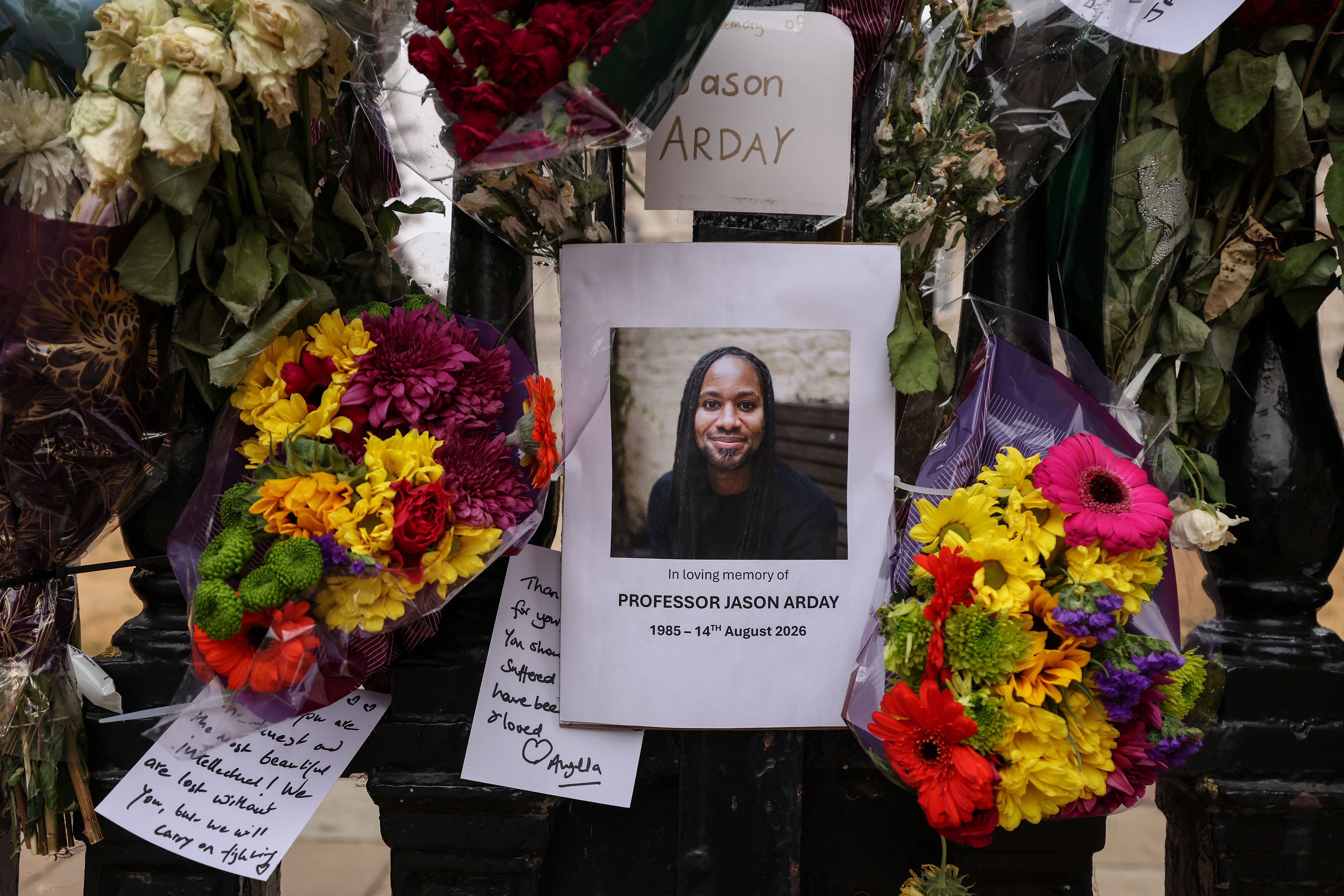 A photo (C) of late Cambridge professor Jason Arday is pictured along with floral tributes, attached to the fencing by supporters around the Senate House at the University of Cambridge, in the town of Cambridge, eastern England on August 18, 2026, following his death at age 41 on August 14.