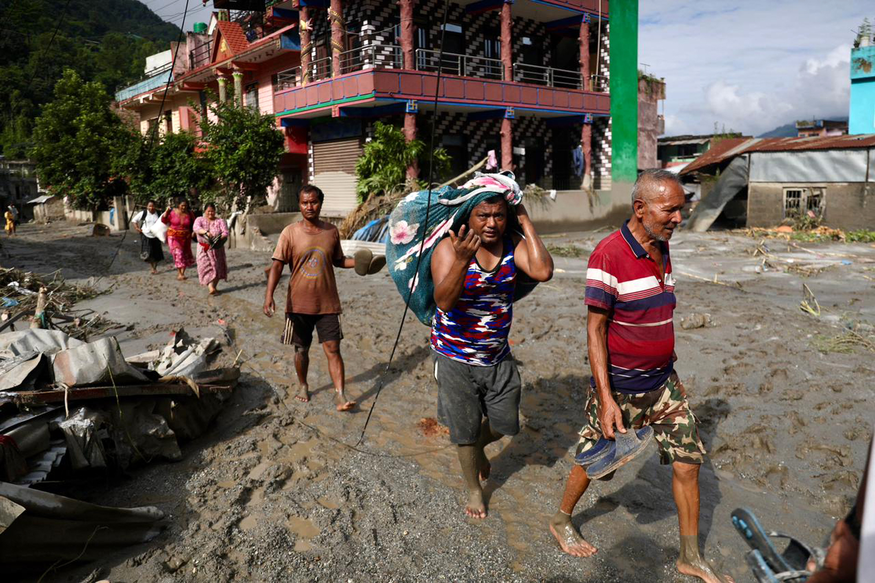 Local residents walk past houses lying deluged in sludge after flash floods near Devighat, Bidur Municipality in Nepal's Nuwakot district on August 27, 2026.