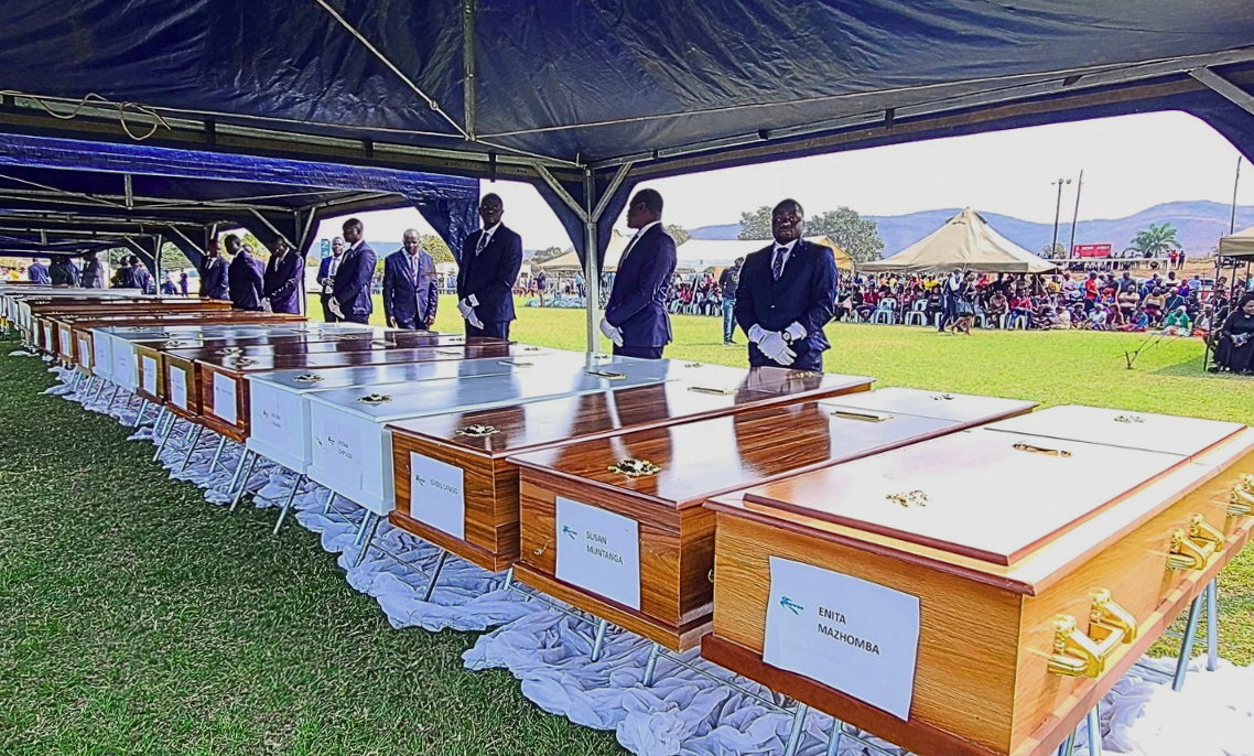 A pallbearer stands next to a line of coffins during a memorial service for victims of a passenger ferry that capsized on Lake Kariba