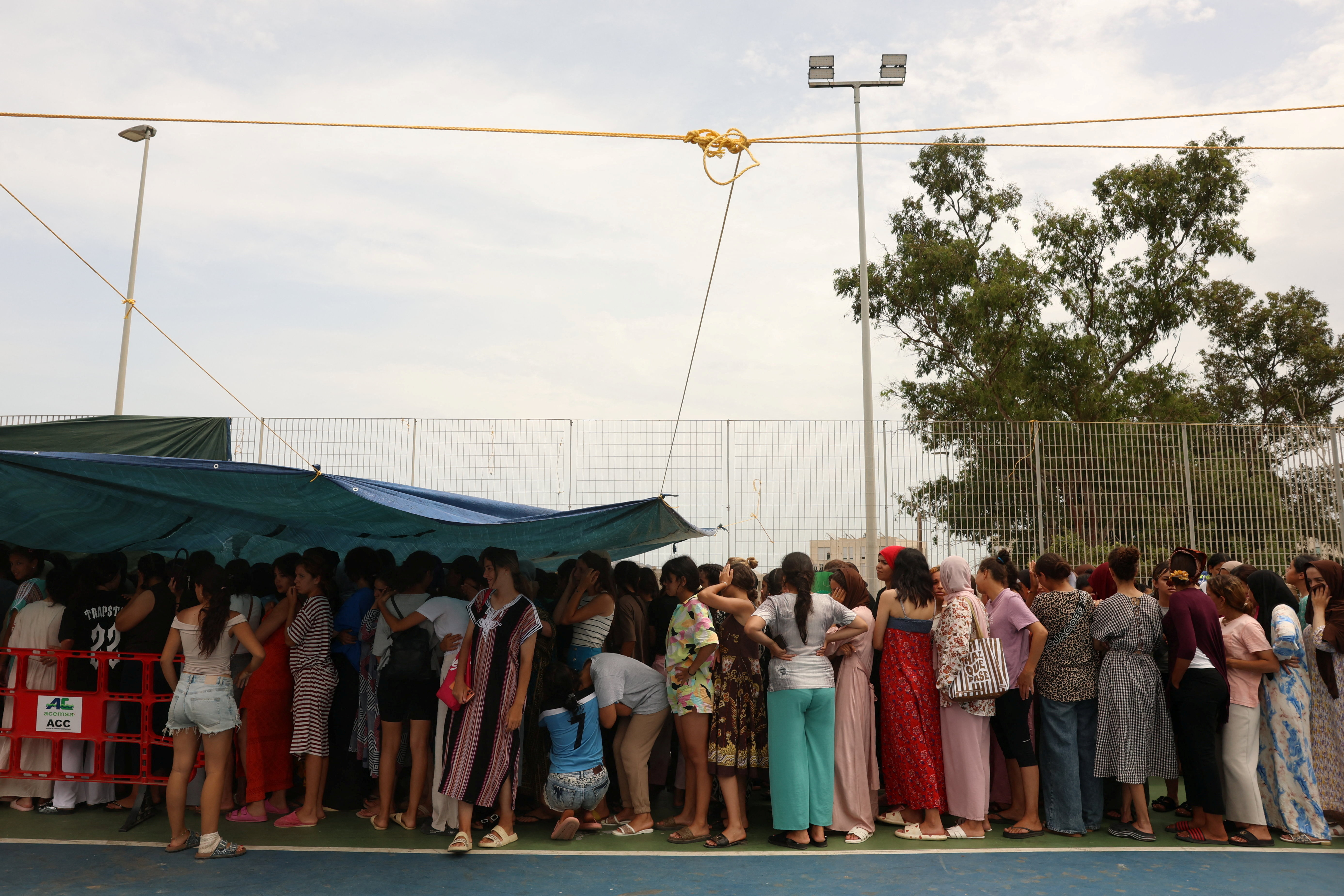 Migrant women and children await for a donated meal in a sports field set up by local residents as an improvised shelter for women and children, following a mass crossing of migrants from Morocco, in the neighboorhood el Principe in Spain's North African enclave of Ceuta, August 19, 2026. REUTERS/Violeta Santos Moura