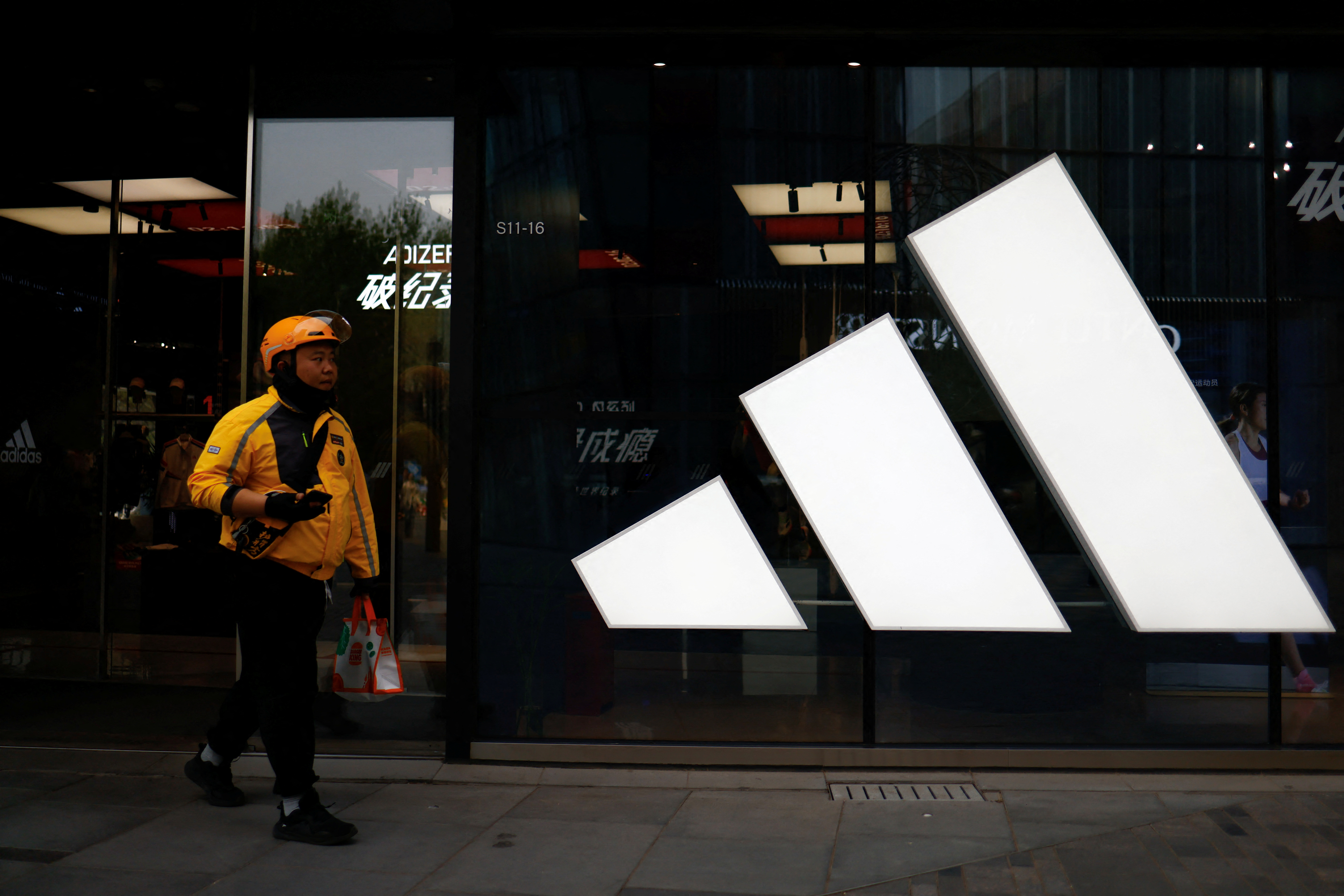 A delivery worker walks past an Adidas store at a shopping compound in Beijing, China April 9, 2025. REUTERS/Tingshu Wang