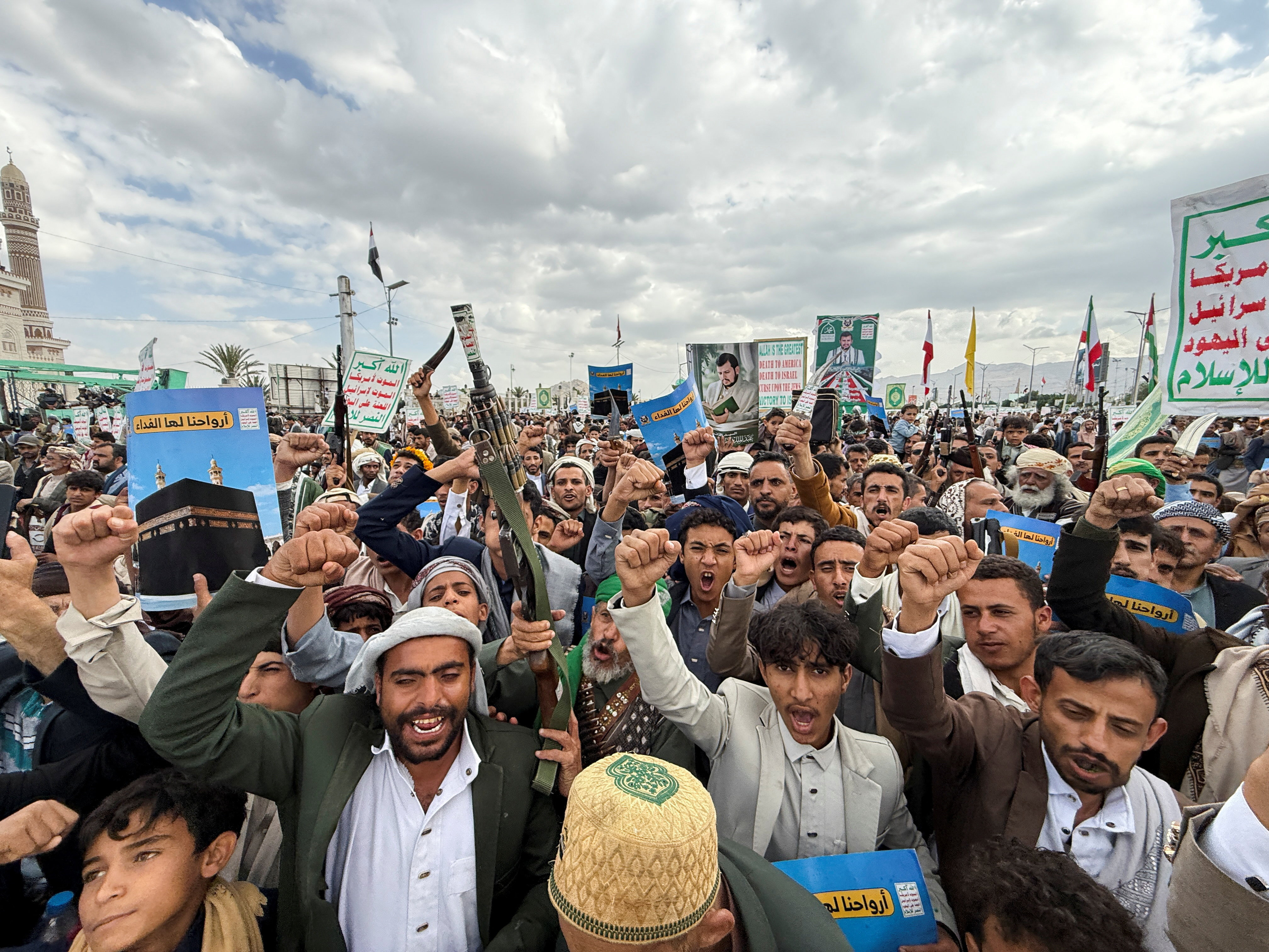 A crowd of men waving flags and raising rifles at a rally in Sanaa