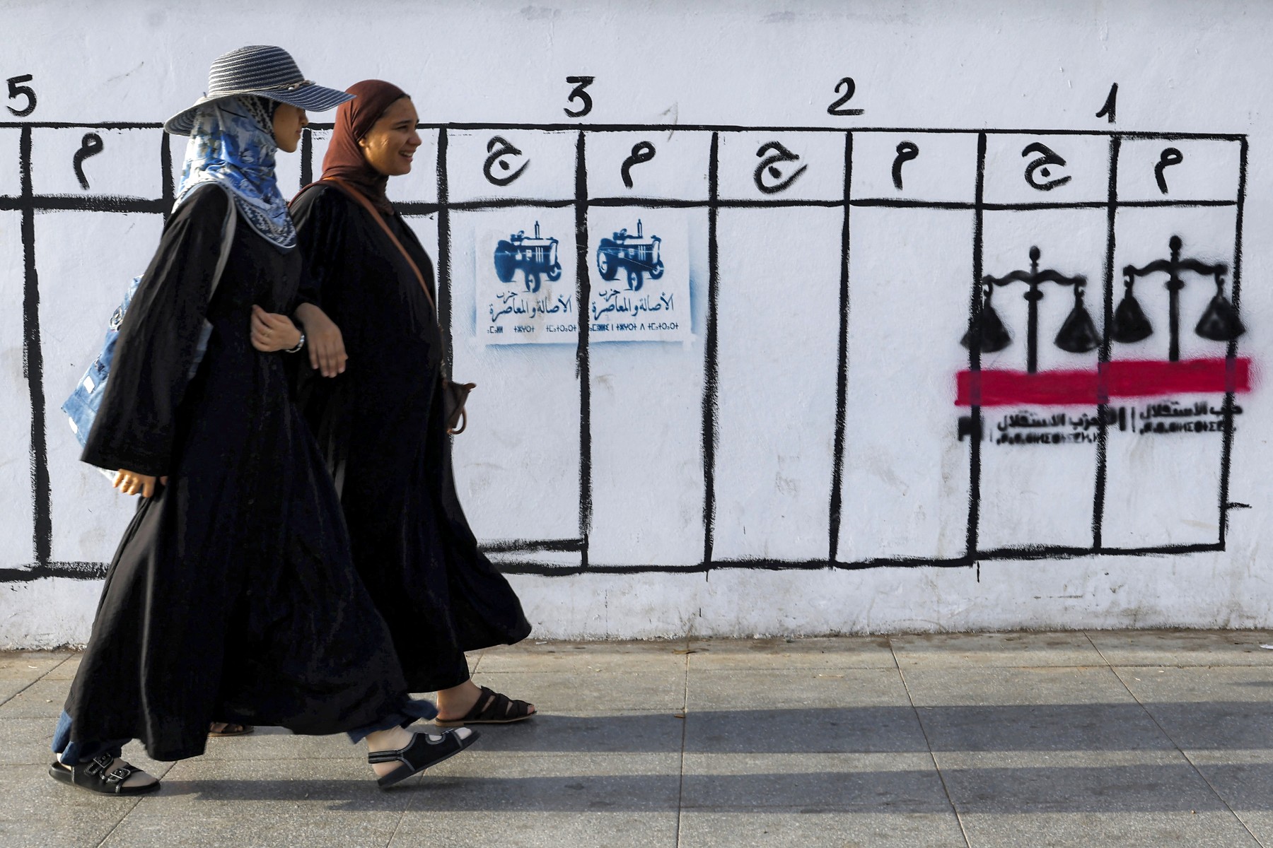 Women walk past electoral symbols used by political parties in Morocco’s legislative election in Rabat on September 14, 2026 [Abdel Majid BZIOUAT / AFP]