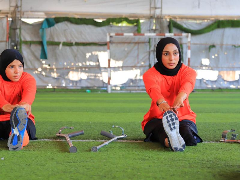Two girls with amputated legs stretch on a football field