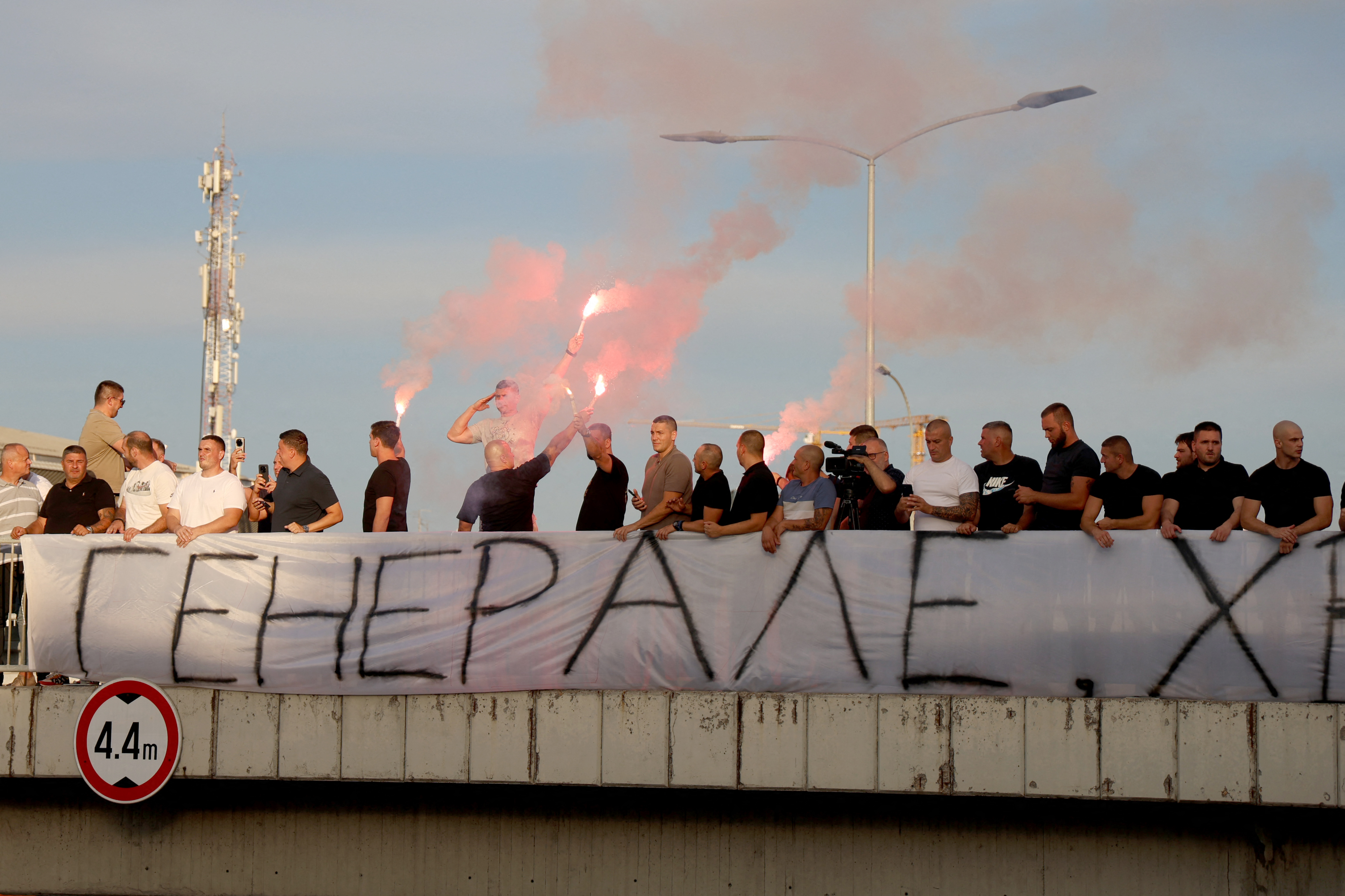 A group of people gathered on a footbridge over a motorway hold a banner reading "General" and light flares as they greet a convoy carrying the body of Bosnian Serb war criminal Ratko Mladic as it passes through Belgrade, Serbia, on September 3, 2026.