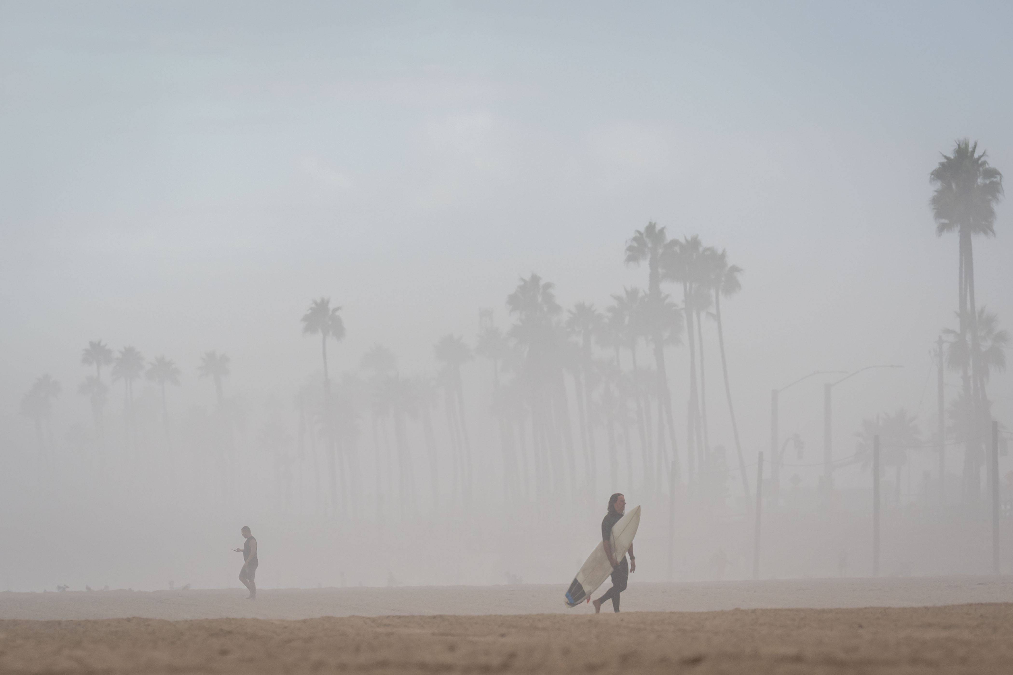 A surfer walks through thick humidity as large waves from Hurricane Marie break on the shore, Monday, Sept. 7, 2026, on Huntington Beach, southern Calif. (AP Photo/Ethan Swope)