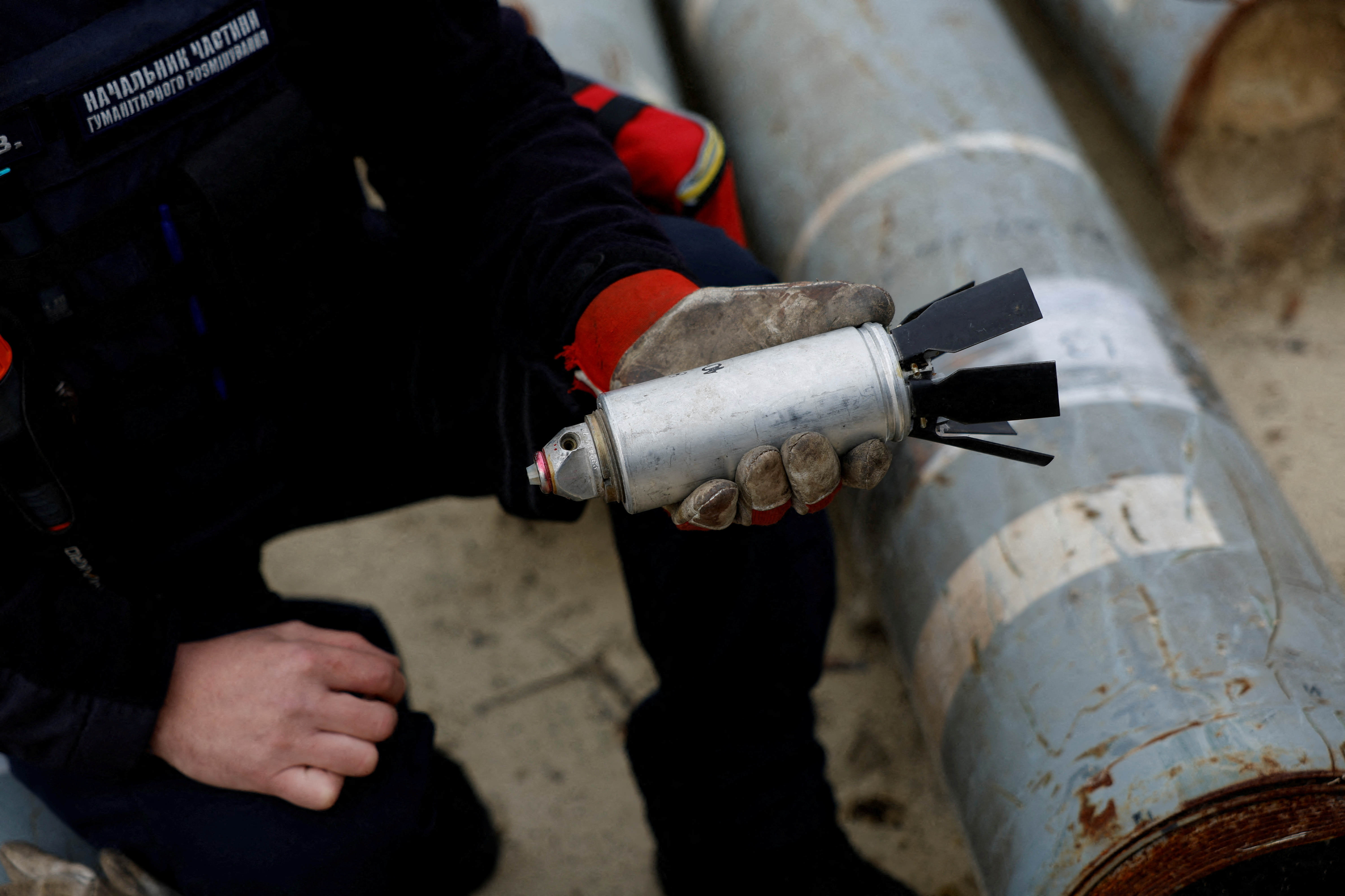 Ukrainian military serviceman Igor Ovcharruck holds a defused cluster bomb from an MSLR missile, among a display of pieces of rockets used by Russian army, that a Ukrainian munitions expert said did not explode on impact, in the region of Kharkiv, Ukraine, October 21, 2022. [Clodagh Kilcoyne/Reuters]