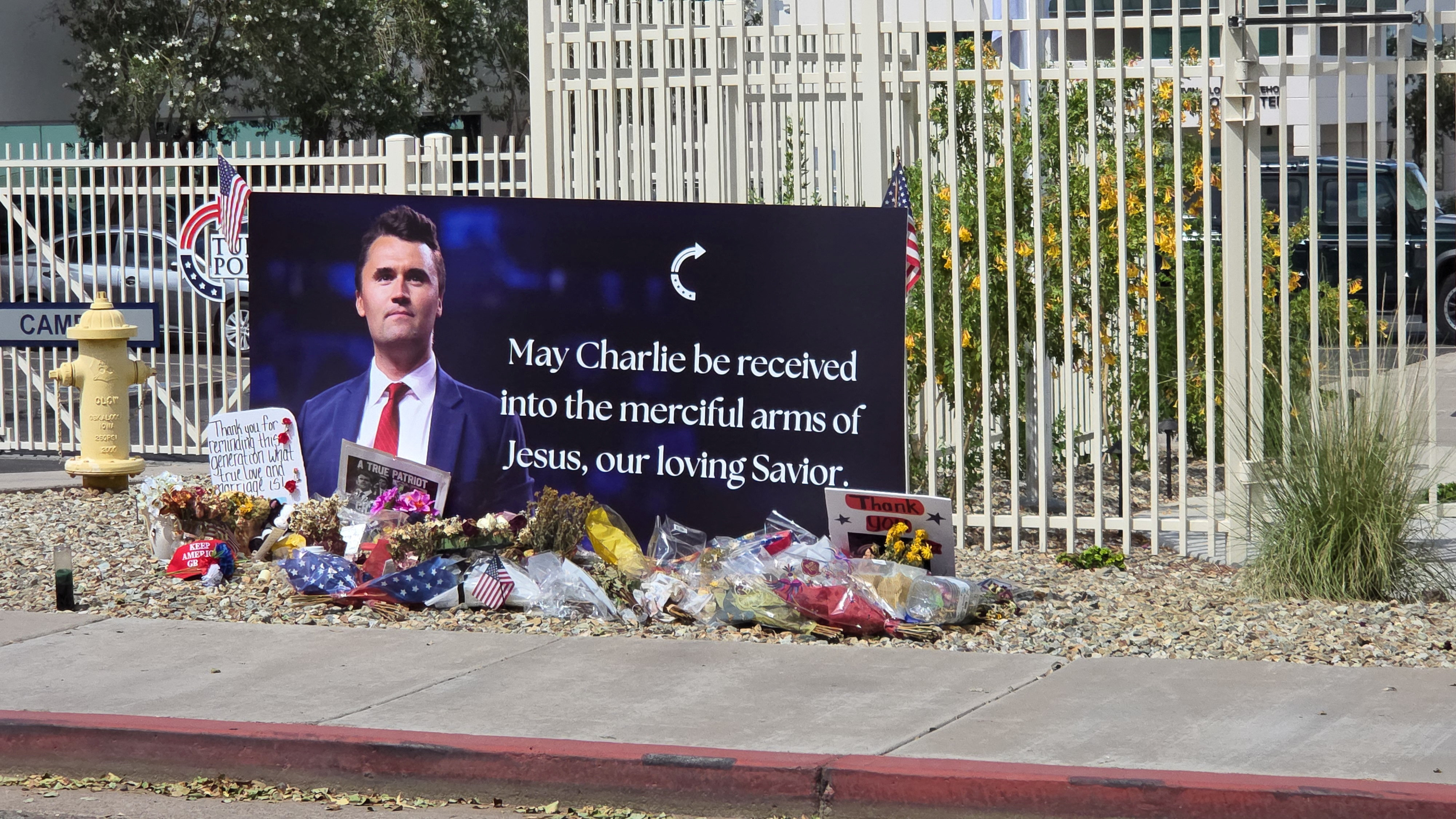 A memorial display of flowers, candles and photographs left for Charlie Kirk on the pavement outside a building.