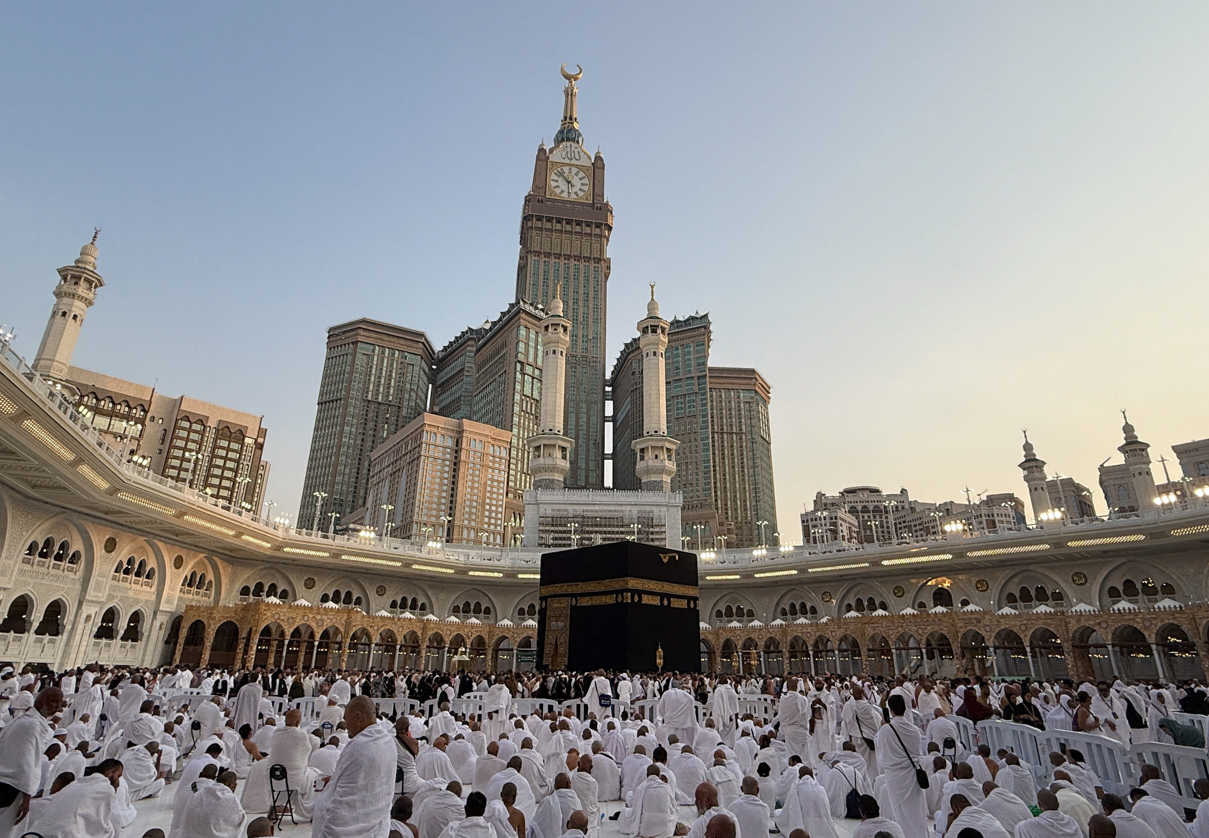 Crowds of pilgrims in white robes move around a large stone structure in a mosque courtyard.