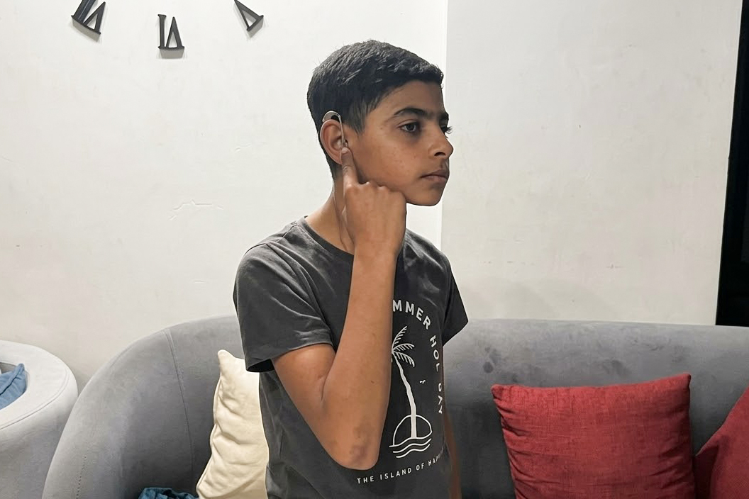 With his father’s help, Kenan al-Saba, a deaf child, attempts to adjust his hearing aid, which has malfunctioned due to the blockade in Gaza.