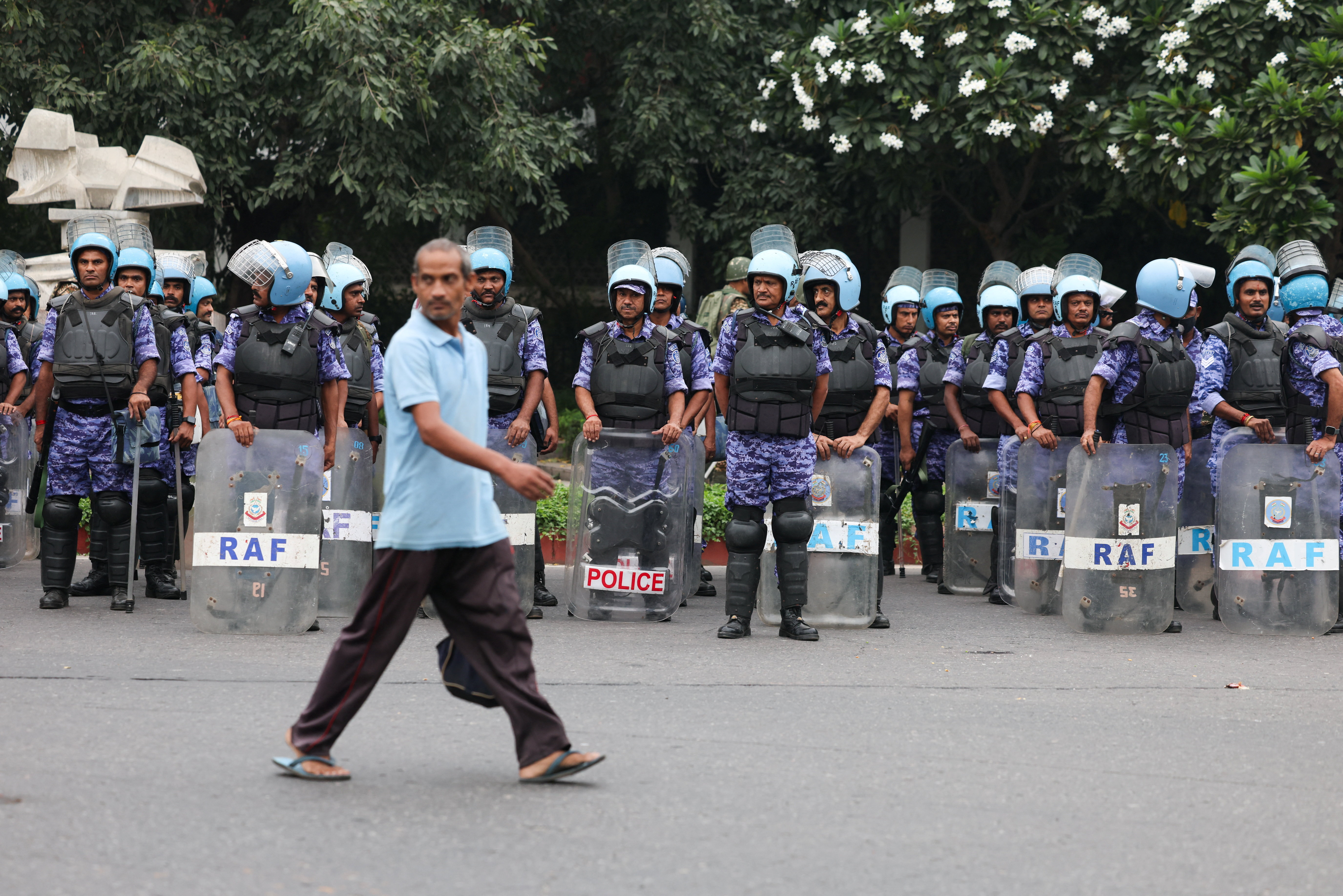 A man walks past members of the Rapid Action Force (RAF) standing guard ahead of a protest planned by the Cockroach Janta Party (CJP) seeking the resignation of India’s Chief Election Commissioner Gyanesh Kumar, in New Delhi, India, October 10, 2026