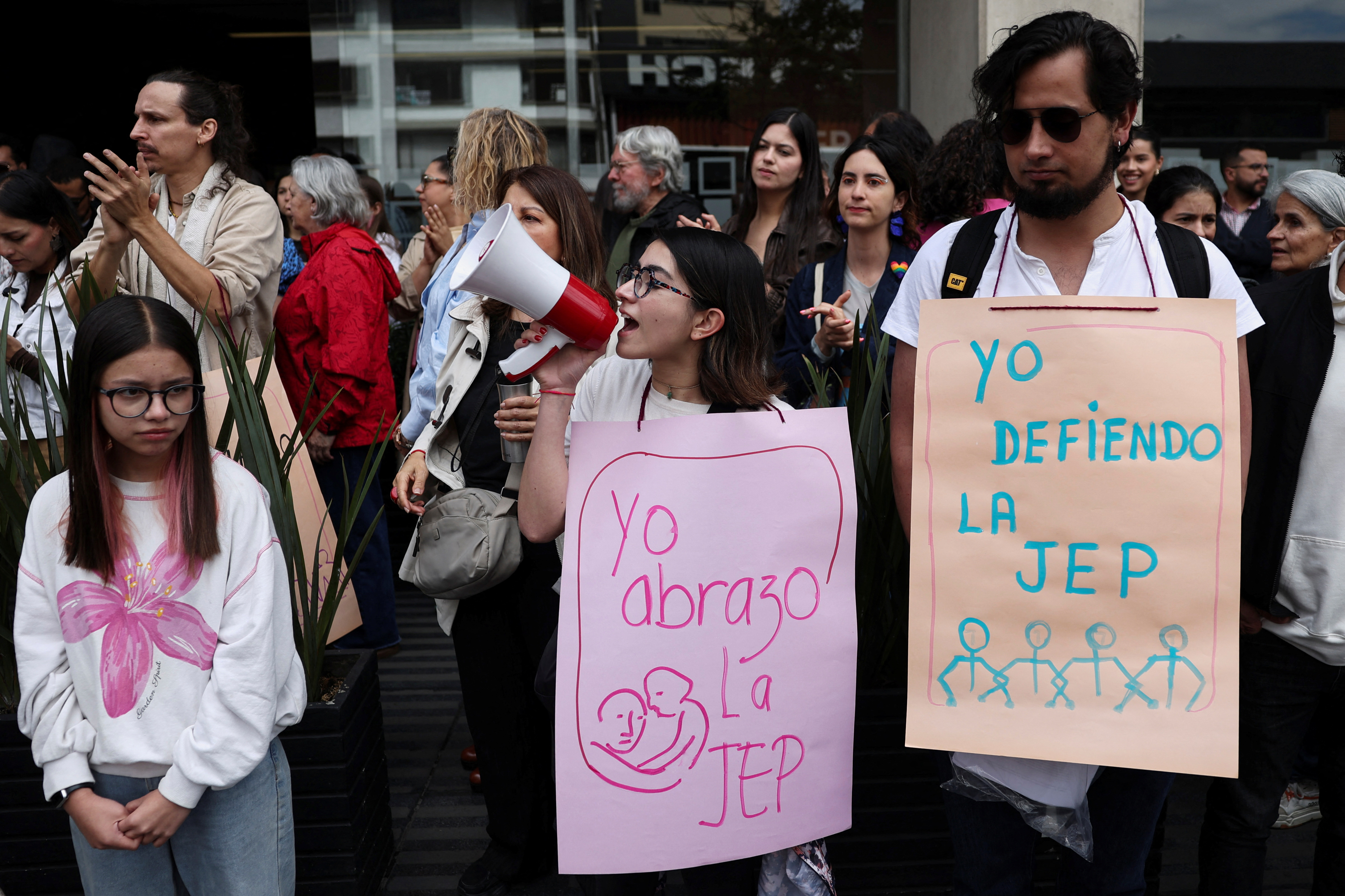 A demonstrator speaks through a megaphone while holding a sign reading "I embrace the JEP", as another holds a sign reading "I defend the JEP", during a protest in support of Colombia's Special Jurisdiction for Peace (JEP), amid proposed budget cuts that could affect the transitional justice court's investigations into human rights abuses committed during the country's armed conflict, outside the JEP headquarters in Bogota, Colombia, October 9, 2026. REUTERS/Luisa Gonzalez