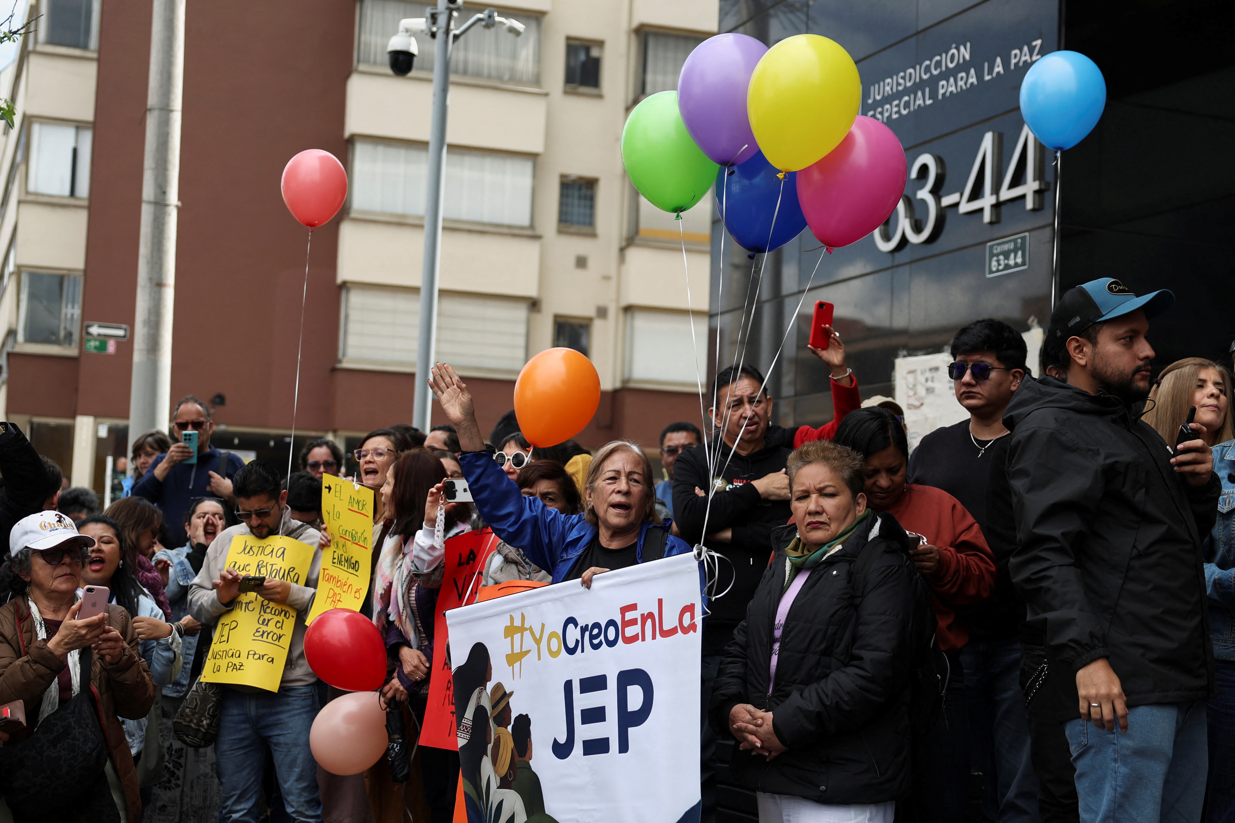 A member of the Mothers of False Positives (MAFAPO) raises her hand while holding a banner reading "I believe in the JEP" alongside demonstrators carrying colorful balloons during a protest in support of Colombia's Special Jurisdiction for Peace (JEP), amid proposed budget cuts that could affect the transitional justice court's investigations into human rights abuses committed during the country's armed conflict, outside the JEP headquarters in Bogota, Colombia, October 9, 2026. REUTERS/Luisa Gonzalez