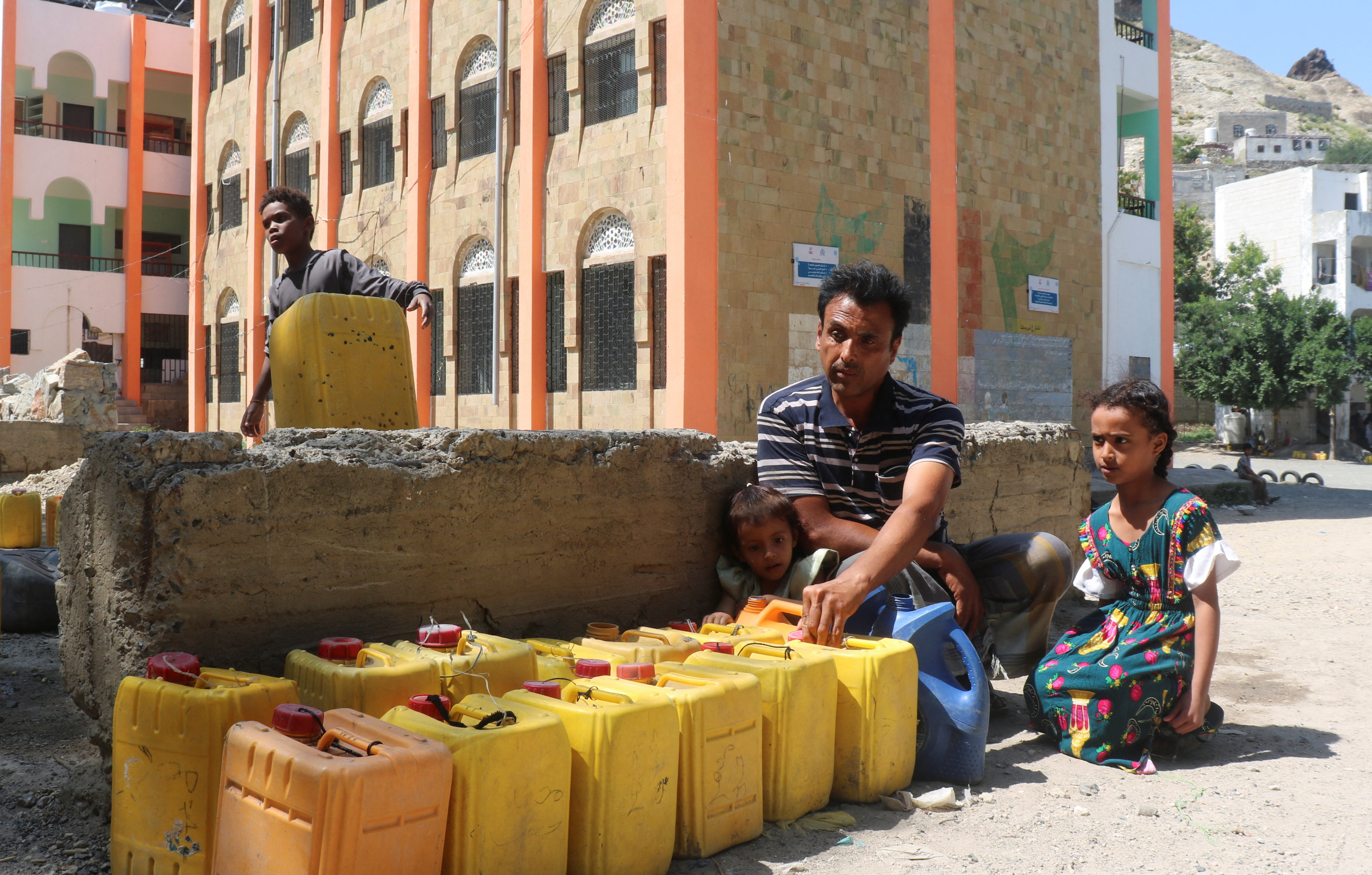 Displaced Yemeni, Ali Hassan, fills a container with water as his daughters sit at a school-turned-shelter in Taiz, Yemen, October 15, 2026. [Ebrahim al-Suhaibi/Reuters]