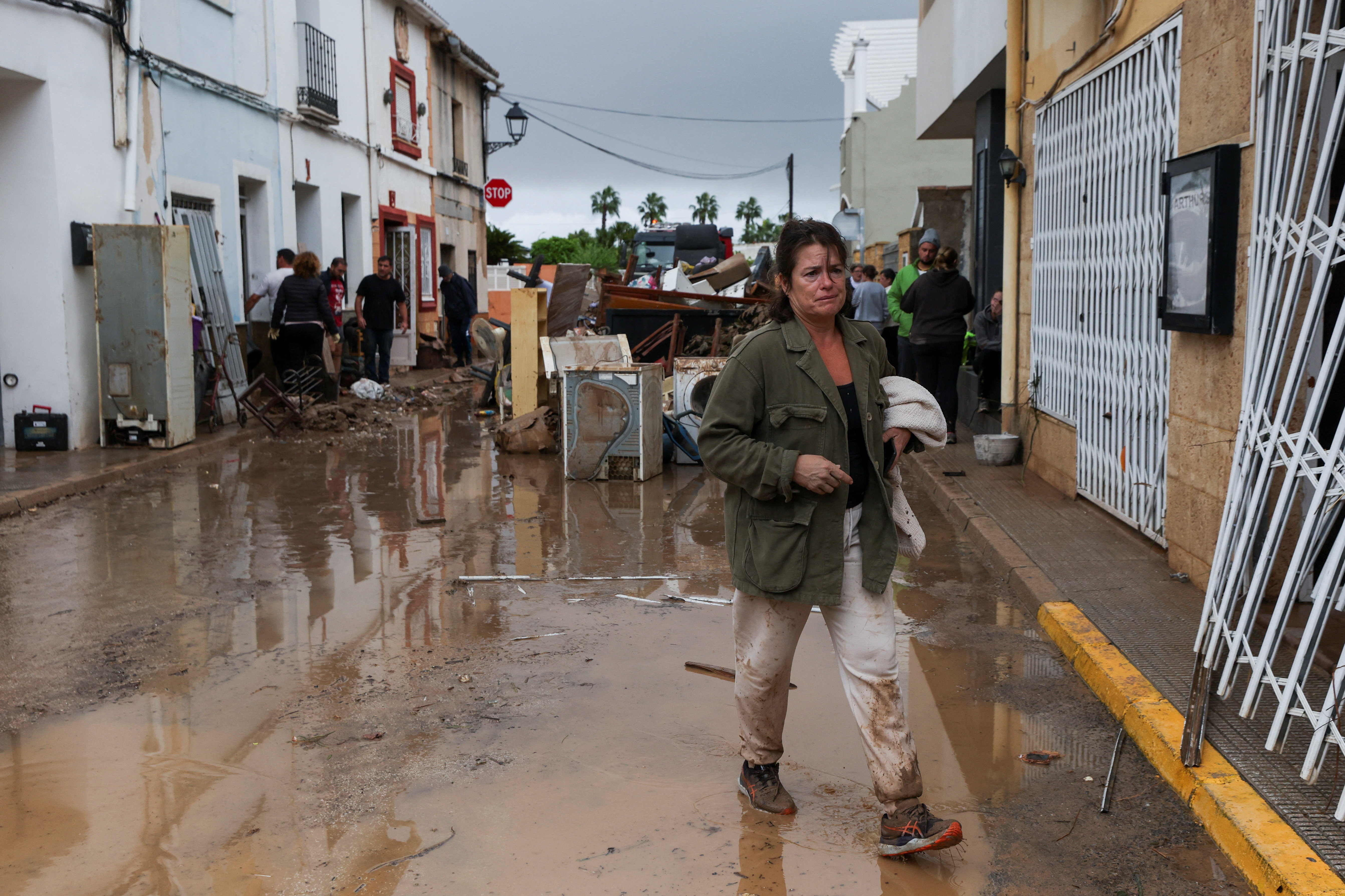 A woman walks on a mud-covered street, following torrential rains, which caused floods in eastern Spain, in Els Poblets, Alicante province, Spain, October 19, 2026 [Eva Manez/Reuters]