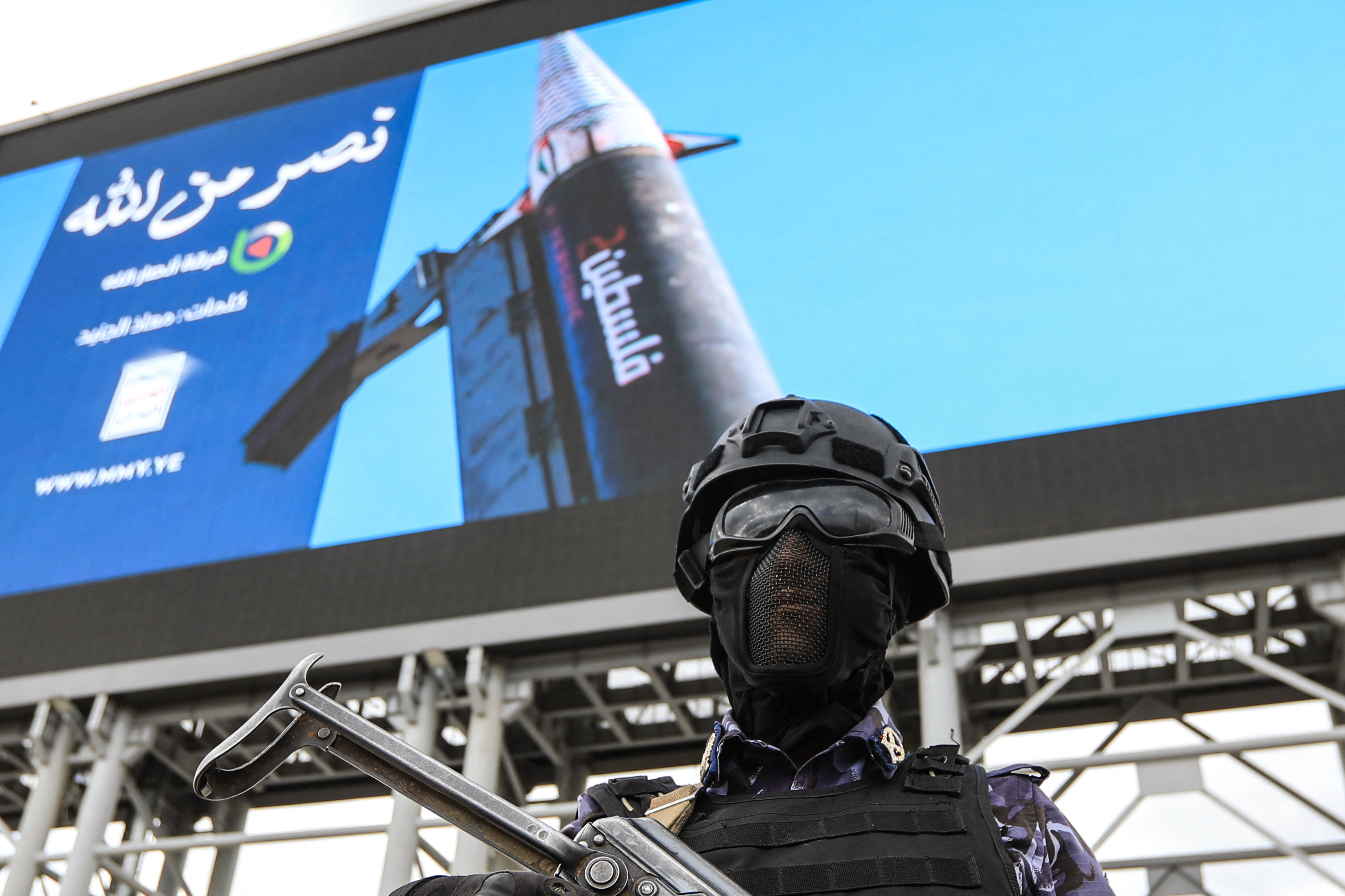 A security personnel officer stands guard in front of a huge image depicting a missile with "Palestine" written on its side, during a rally by supporters of the Iran-backed Houthi movement in solidarity with Iran and Lebanon amid the Middle East war, in the capital Sanaa on April 17, 2026. The Middle East war has created an "unprecedented shock" for the region's economies with no guarantee of a quick recovery, a senior International Monetary Fund official has told AFP. Five of the Gulf's eight oil- and gas-producing countries face a contraction this year, the IMF said in a regional report published on April 16. (Photo by Mohammed HUWAIS / AFP)