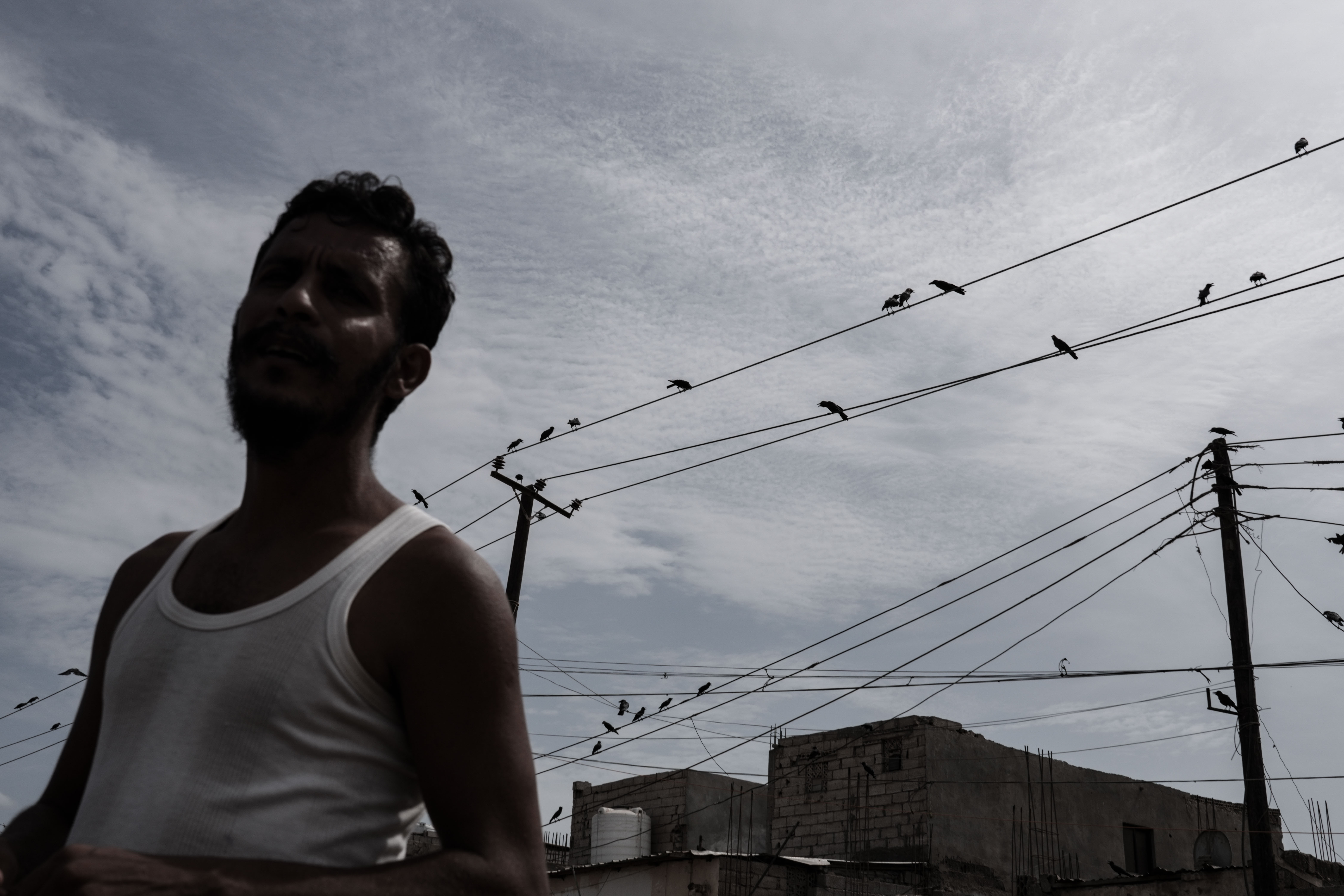 A man walks beneath a web of power lines in a neighborhood in Aden, Yemen. Long and frequent electricity cuts have become part of daily life for residents across the city. Photo: Belal Khaled