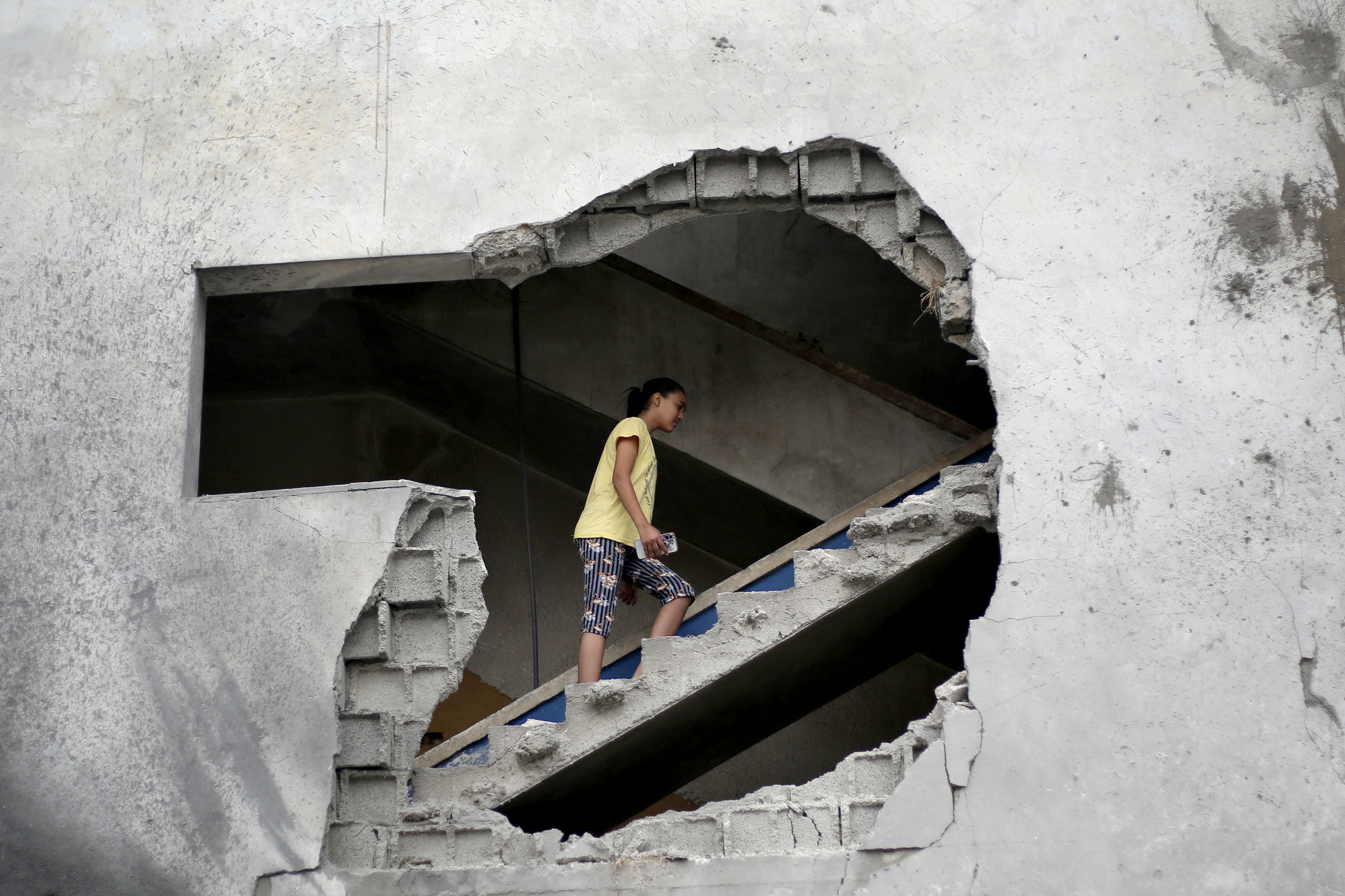 TOPSHOT - A Palestinian is seen through a gapping hole as she walks up a set of stairs to inspect the site of a house targeted in an Israeli airstrikes after the Israeli military warned residents to evacuate last night in Al-Zawayda, central Gaza Strip, on October 11, 2026.