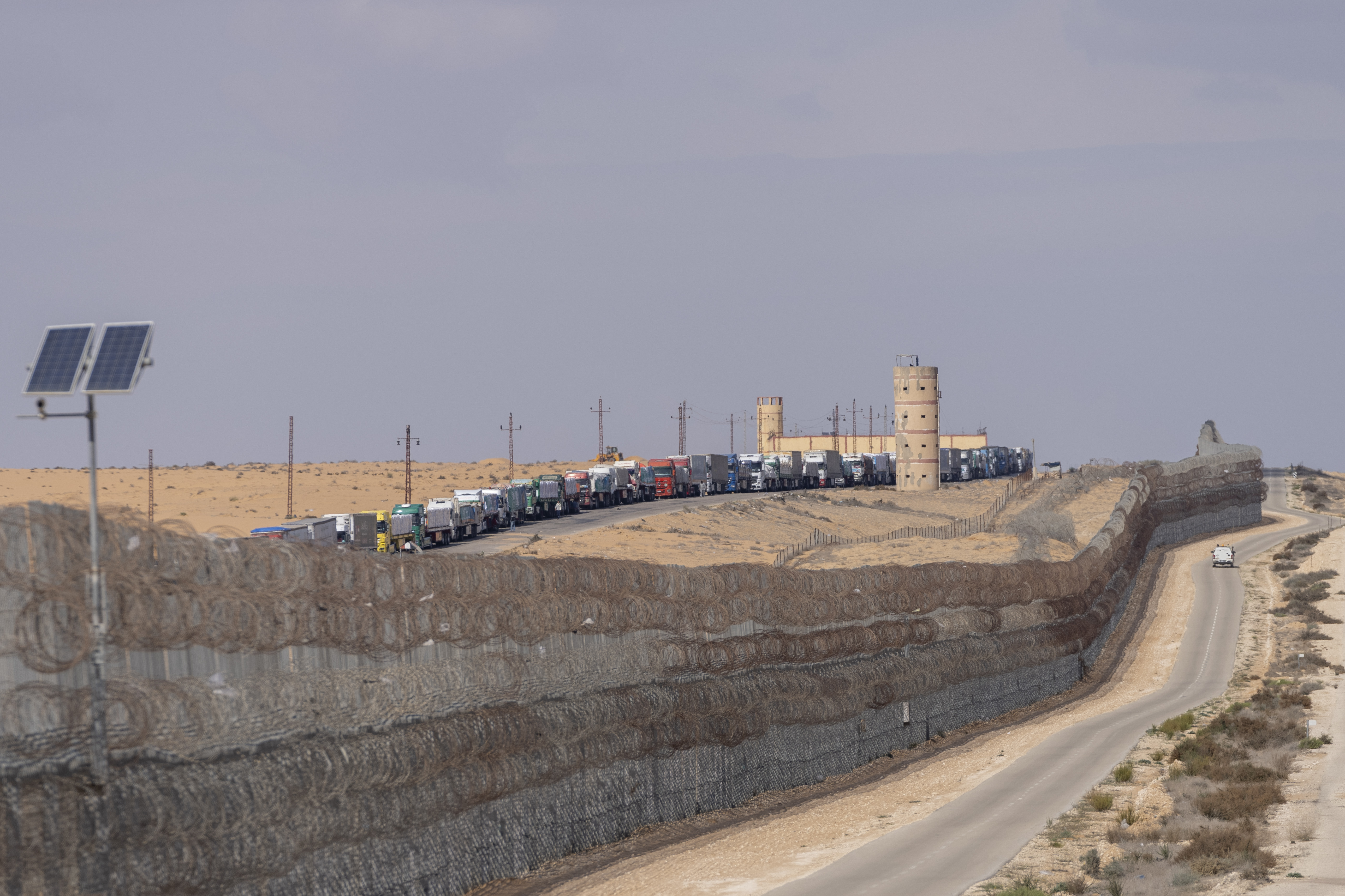 Trucks line up on an area at the Egyptian side as seen from Israeli border at the Nitzana border crossing with Egypt, southern Israel, Wednesday, Feb. 14, 2024. (AP Photo/Ohad Zwigenberg)